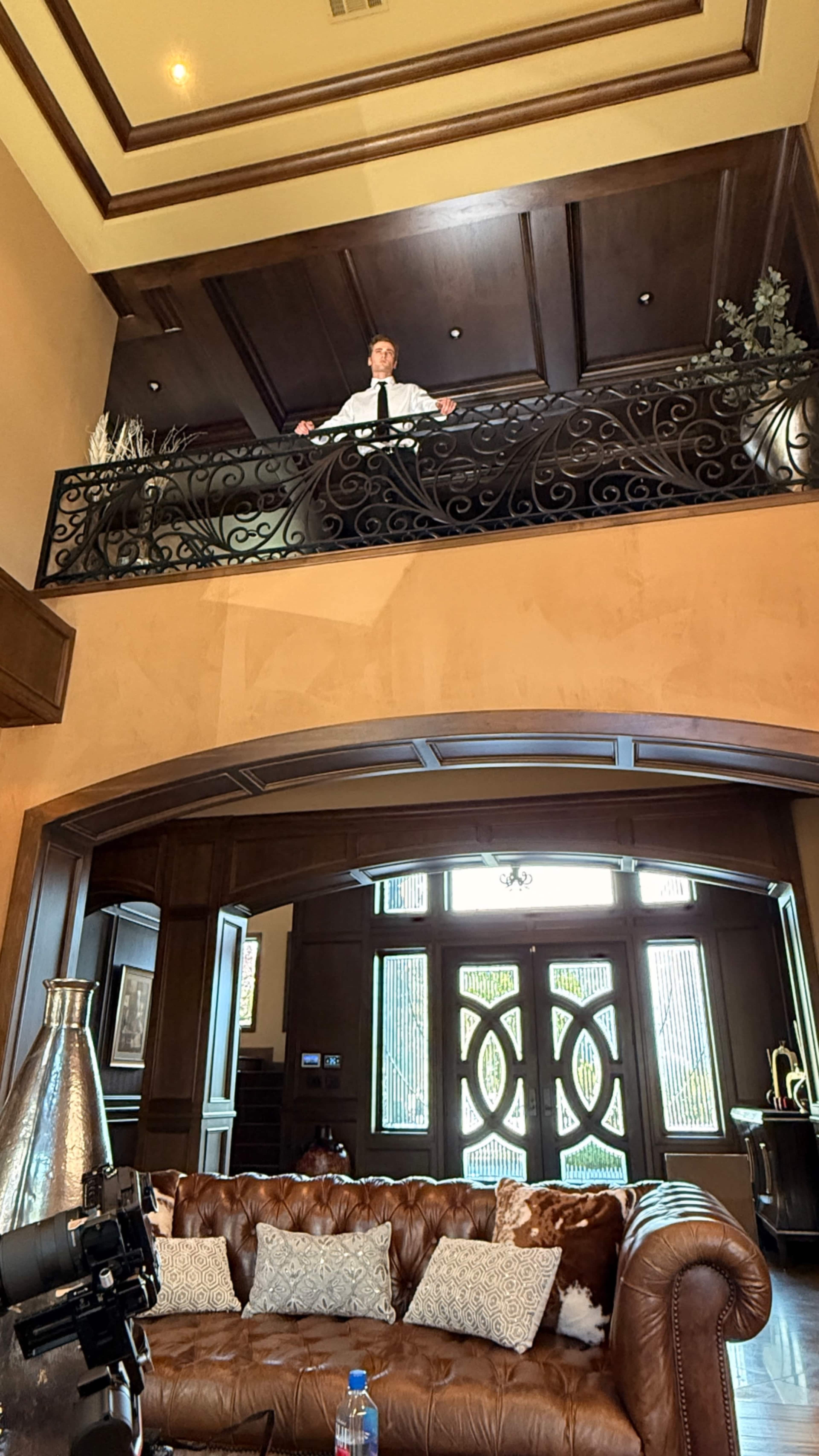 A person stands on a balcony overlooking a living room with a leather sofa and decorative elements.