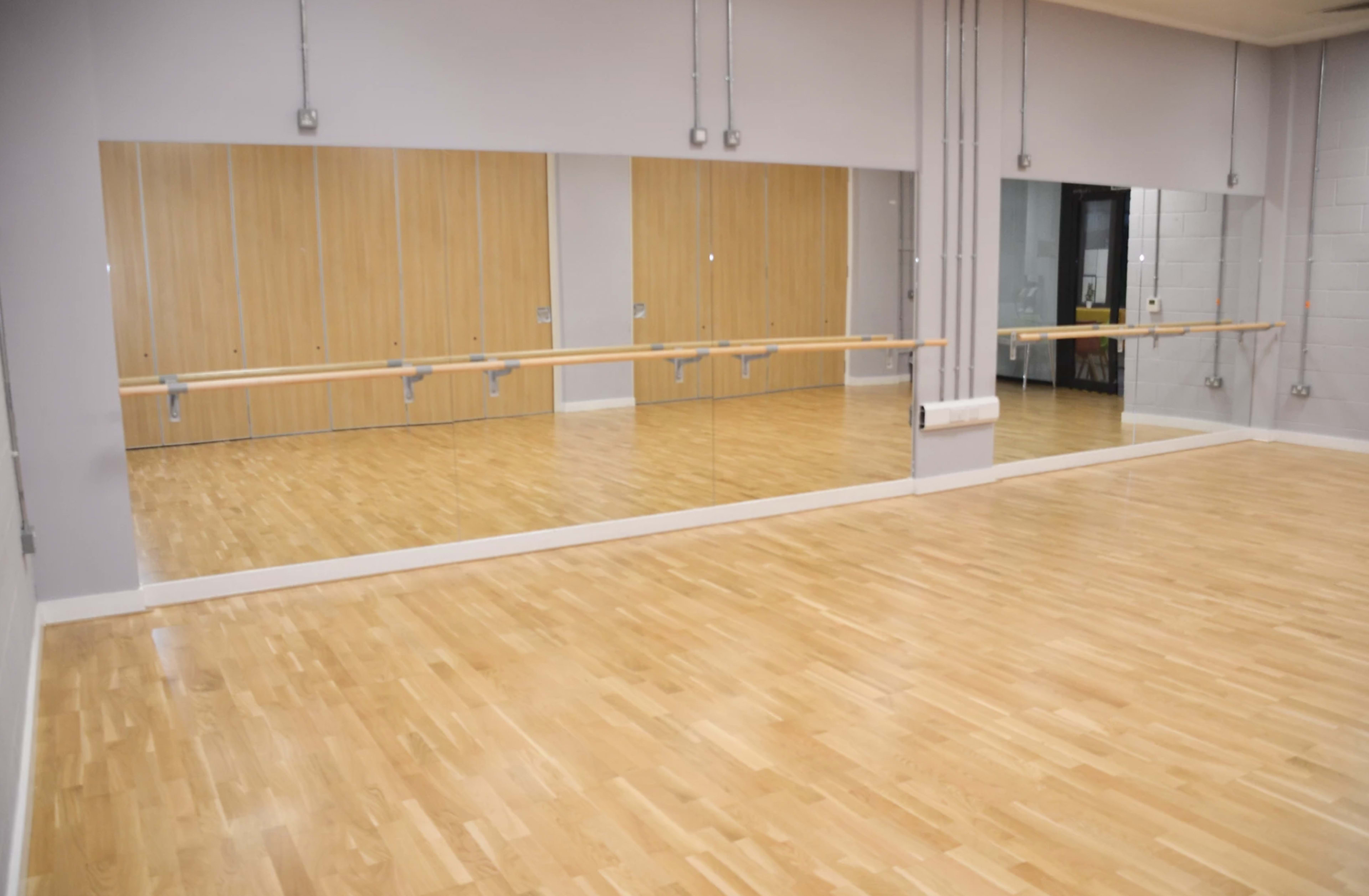 An empty dance studio with wooden floors and large mirrors on one wall.
