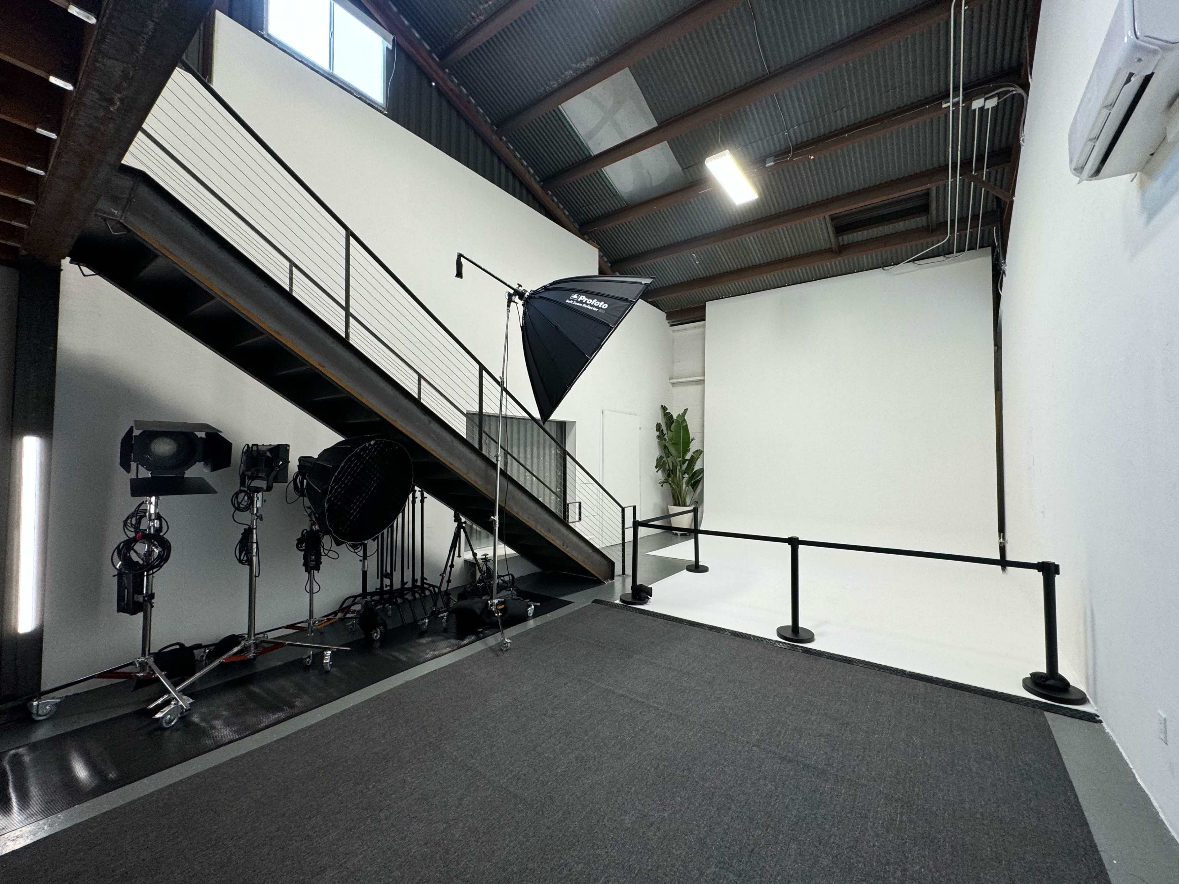An industrial-style studio with a staircase, lighting equipment, and a plain white backdrop.
