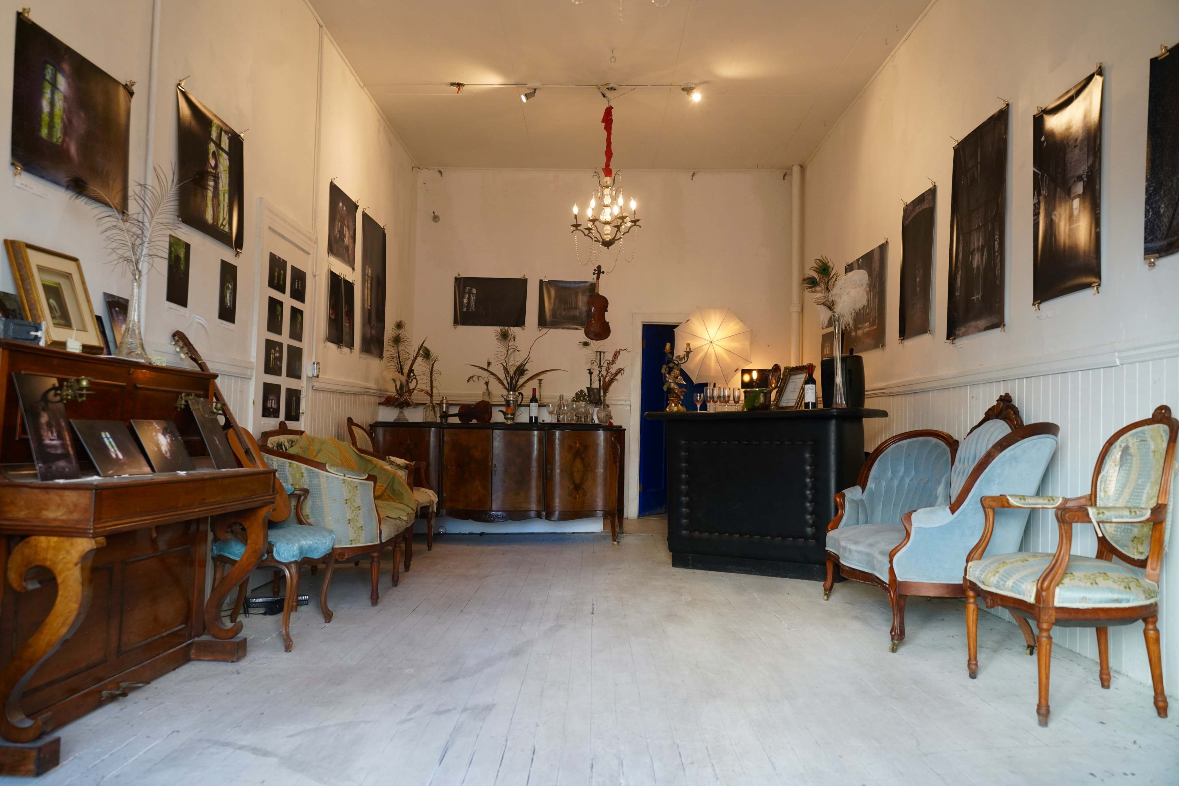 An interior space with vintage furniture, including a wooden desk, two sets of upholstered chairs, and a bar counter against the wall, adorned with framed photographs.
