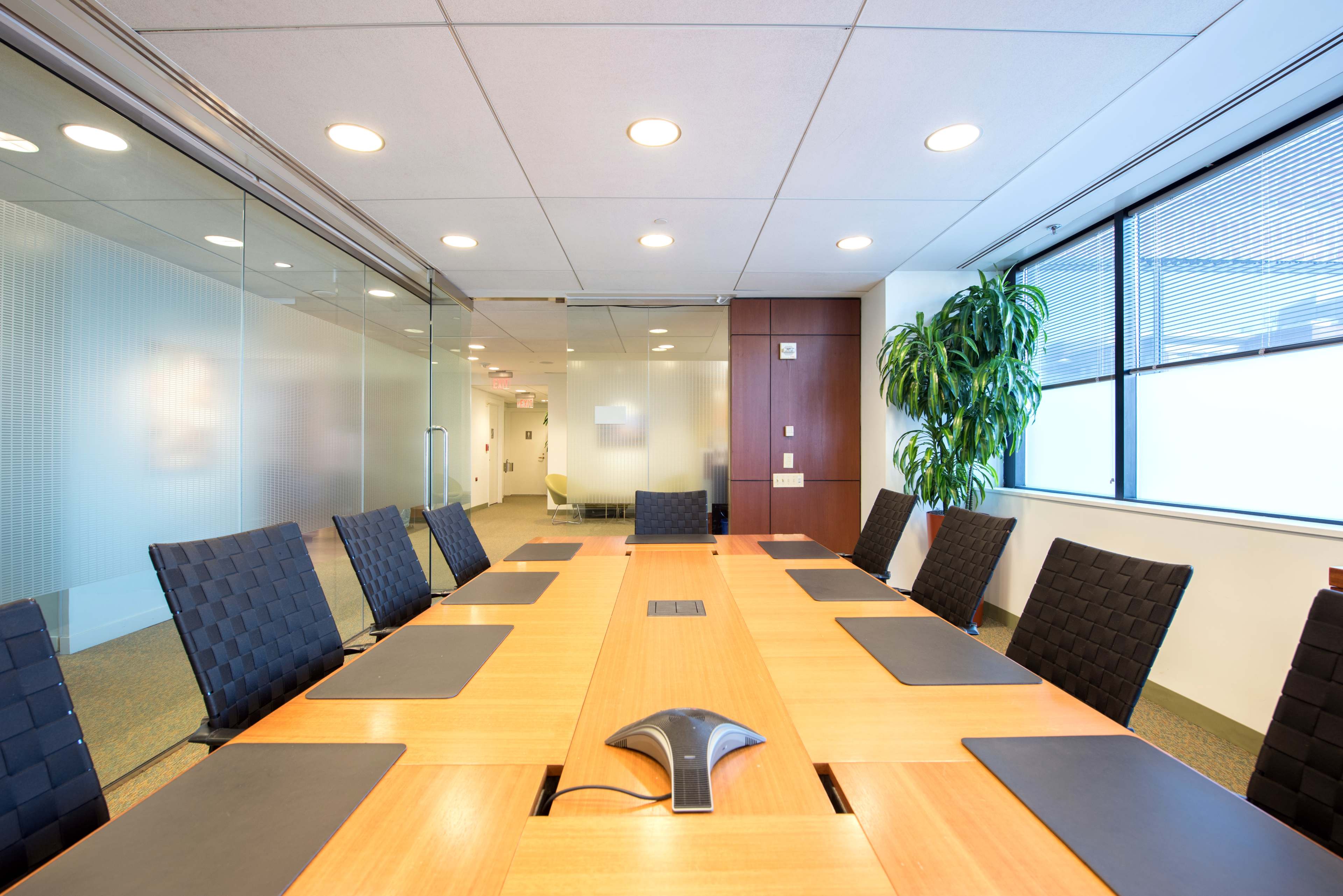 A large conference room features a wooden table surrounded by black leather chairs and is illuminated by overhead lights.