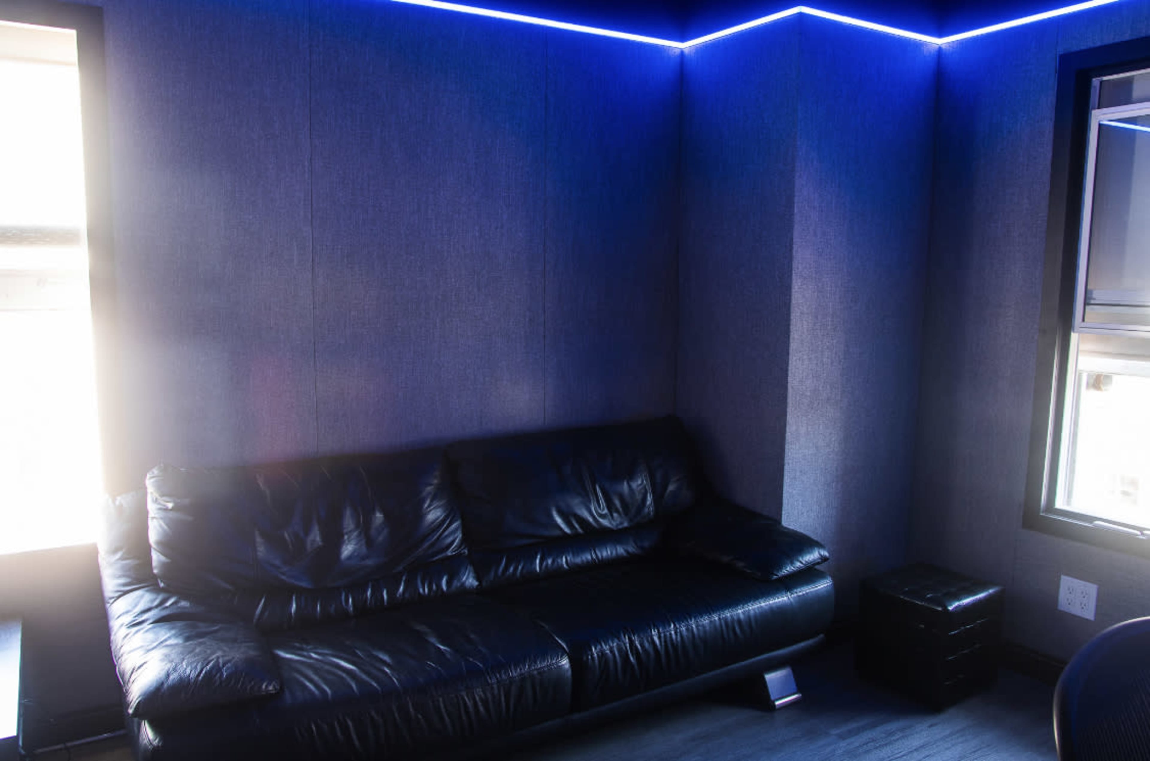 A black leather couch is positioned against a wall with blue LED lighting in a modern room.