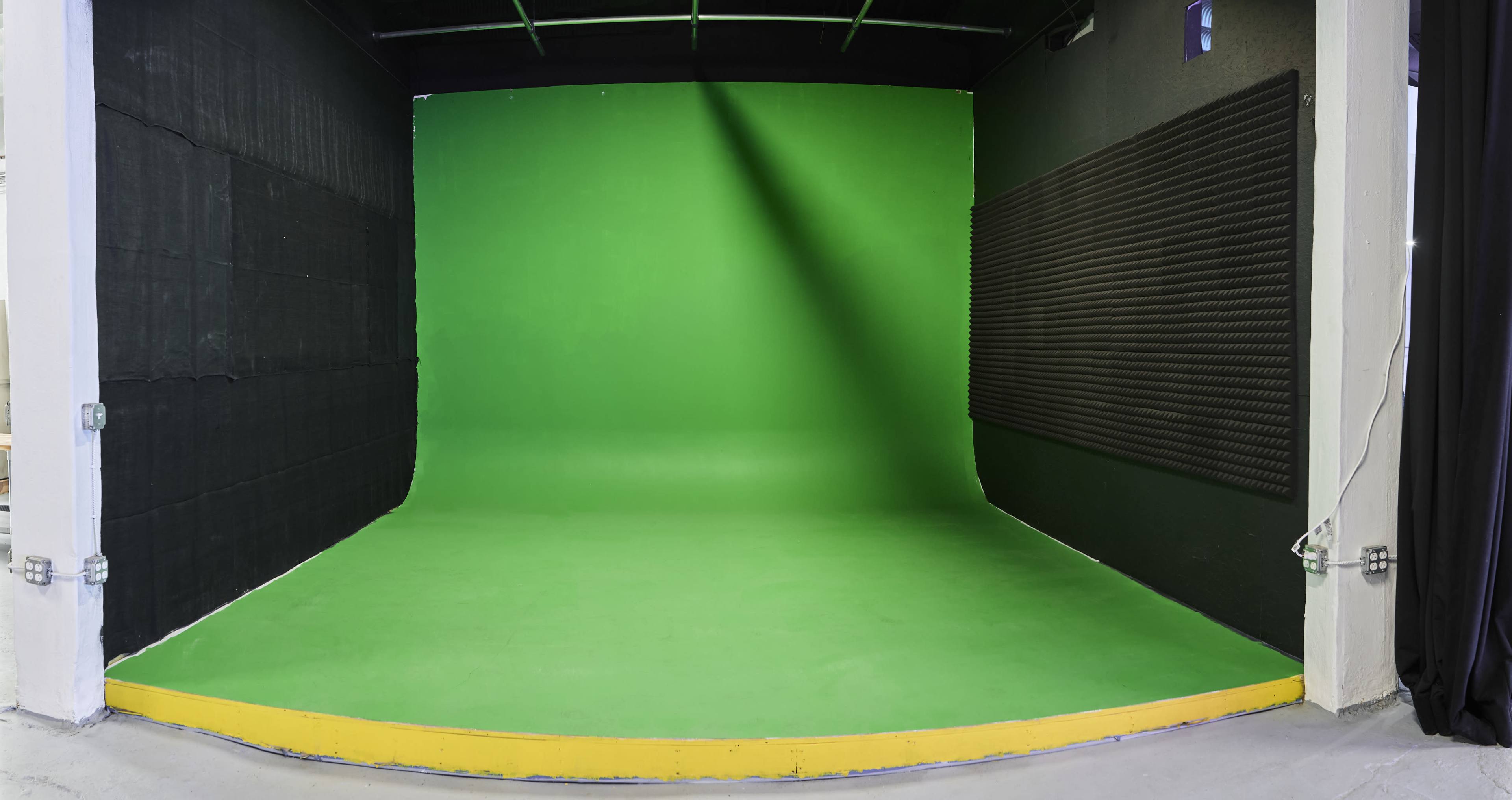 A spacious green screen studio with a smooth green backdrop and black sound-absorbing panels on the walls.