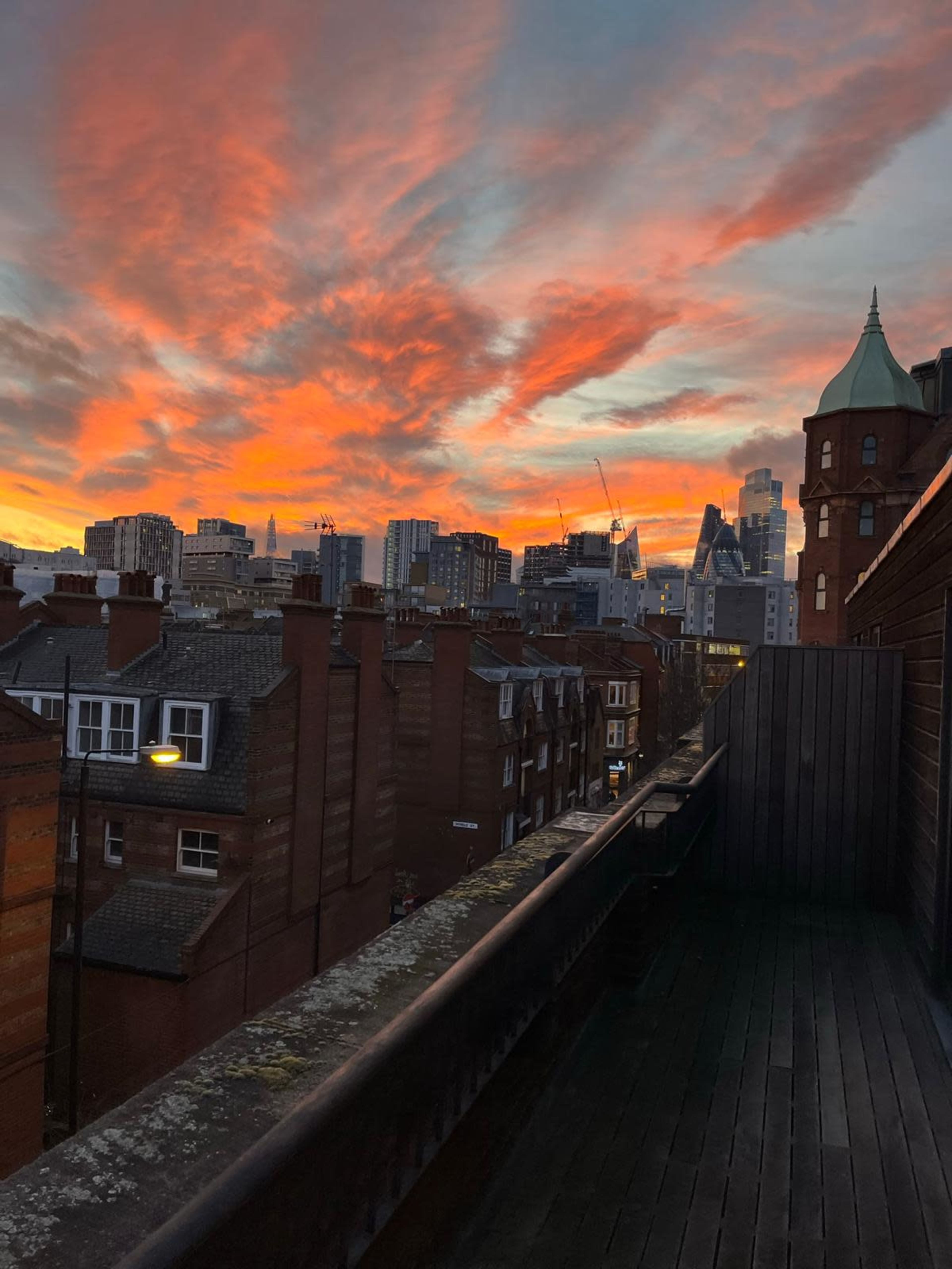 A vibrant sunset over a city skyline, with buildings and rooftops in the foreground.