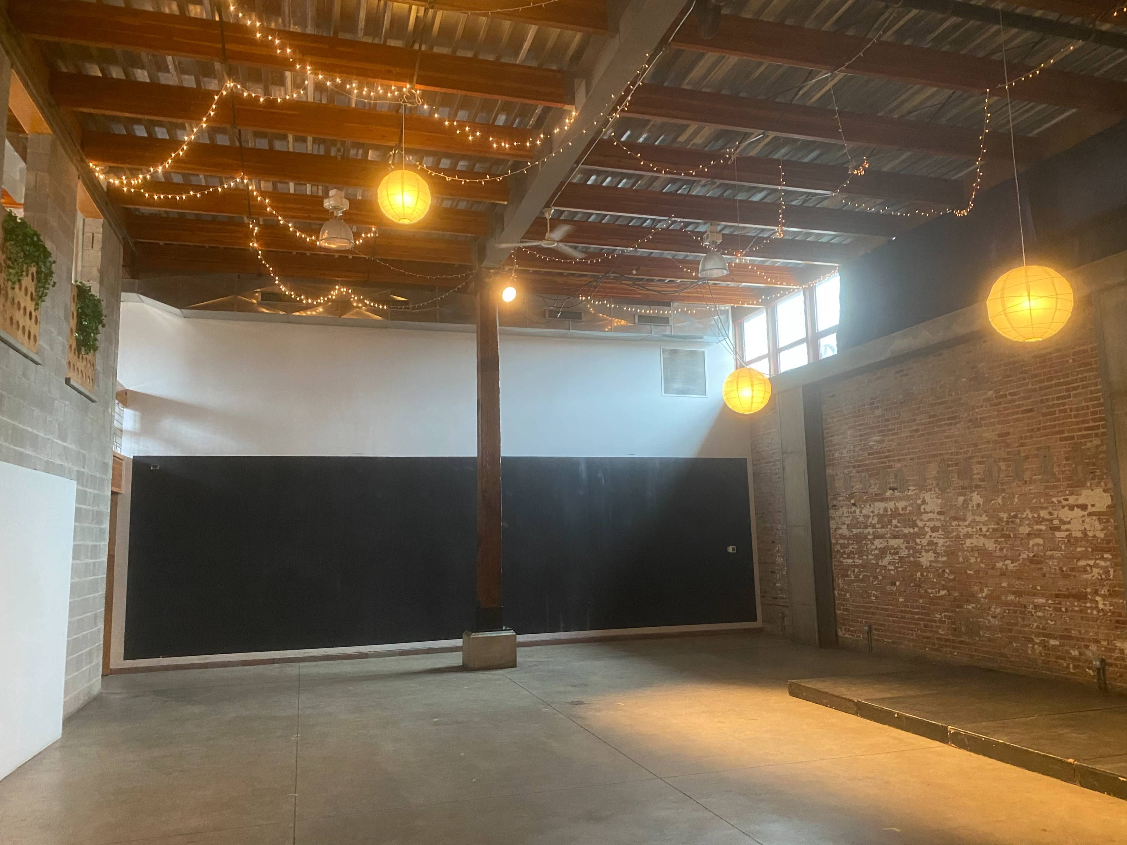 An empty industrial space with exposed brick walls, wooden beams, and pendant lights hanging from the ceiling.