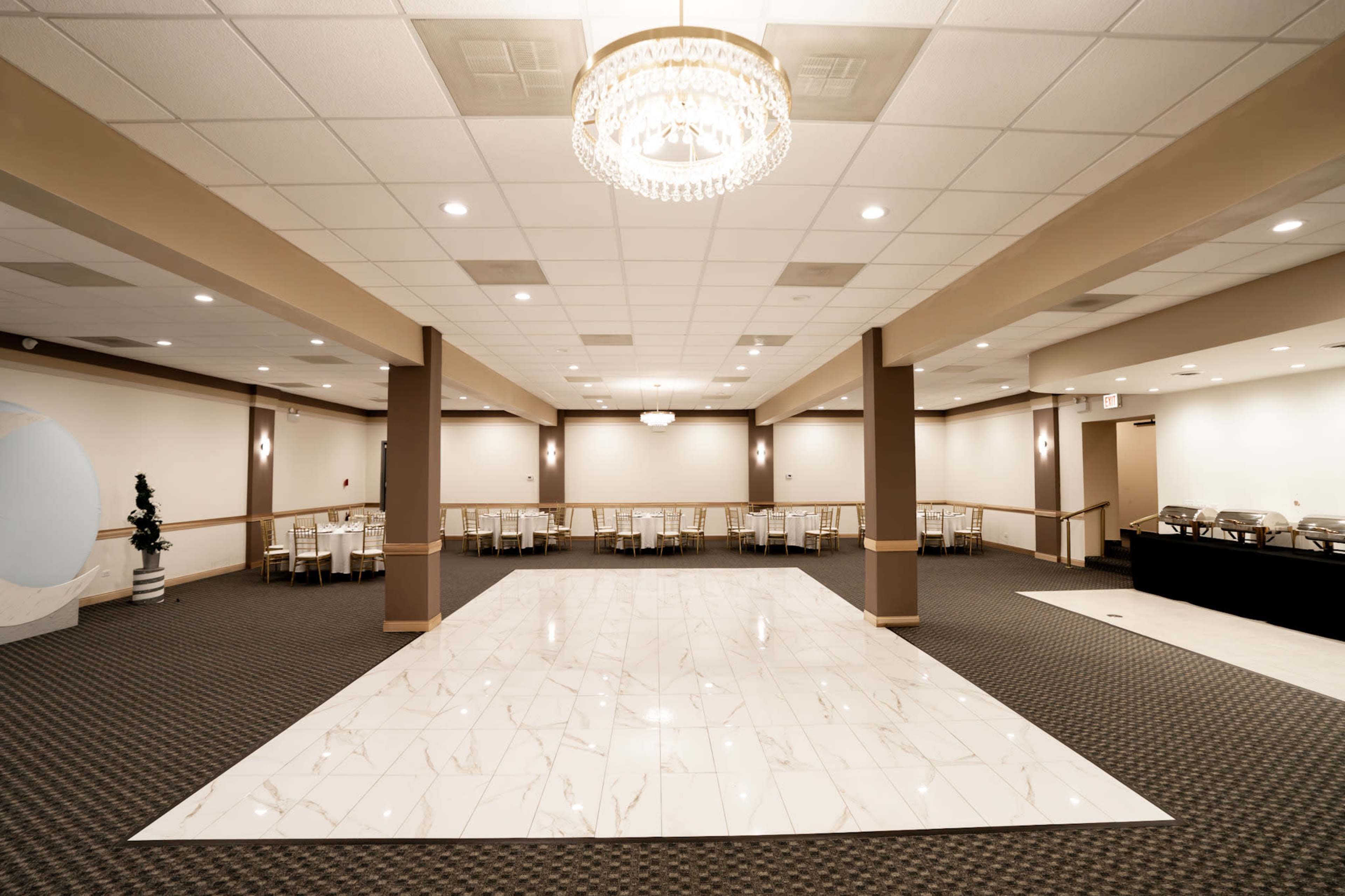 The image shows a spacious event hall featuring a large dance floor with marble tiles, surrounded by neatly arranged tables and chairs.