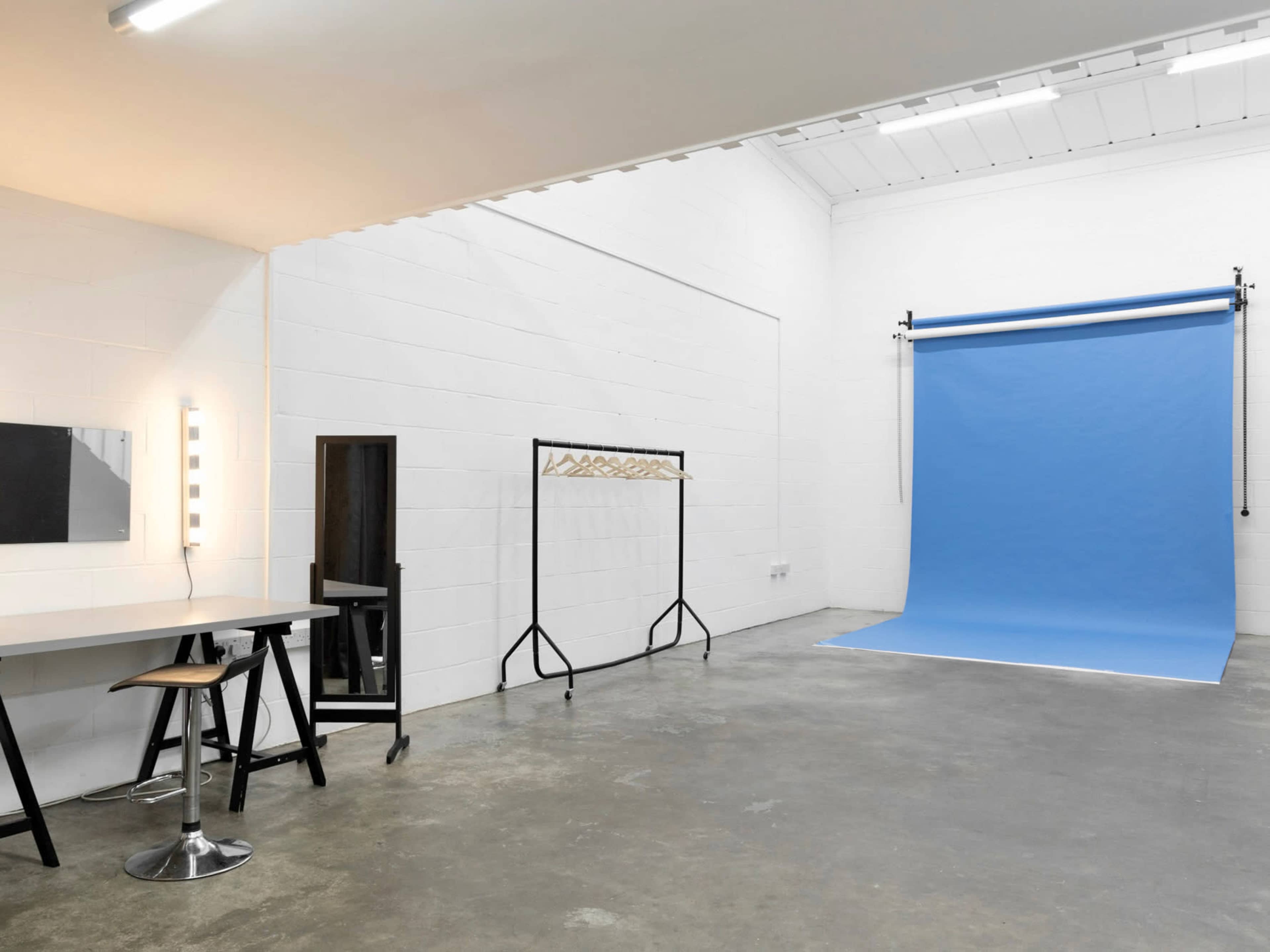 A photography studio with a blue backdrop, a mirror, and a makeup station.