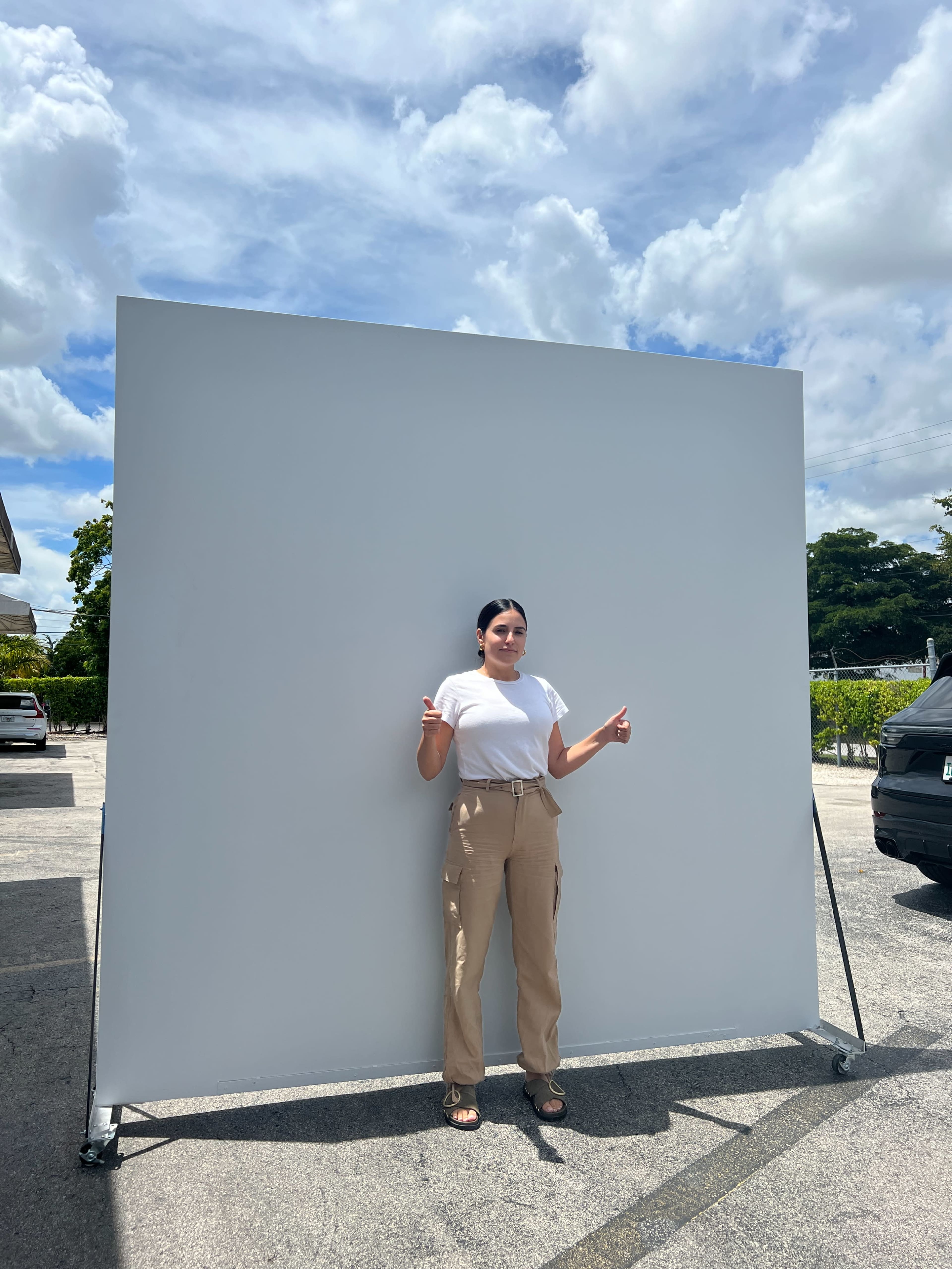 A person stands in front of a blank gray backdrop under a cloudy sky in an outdoor setting.