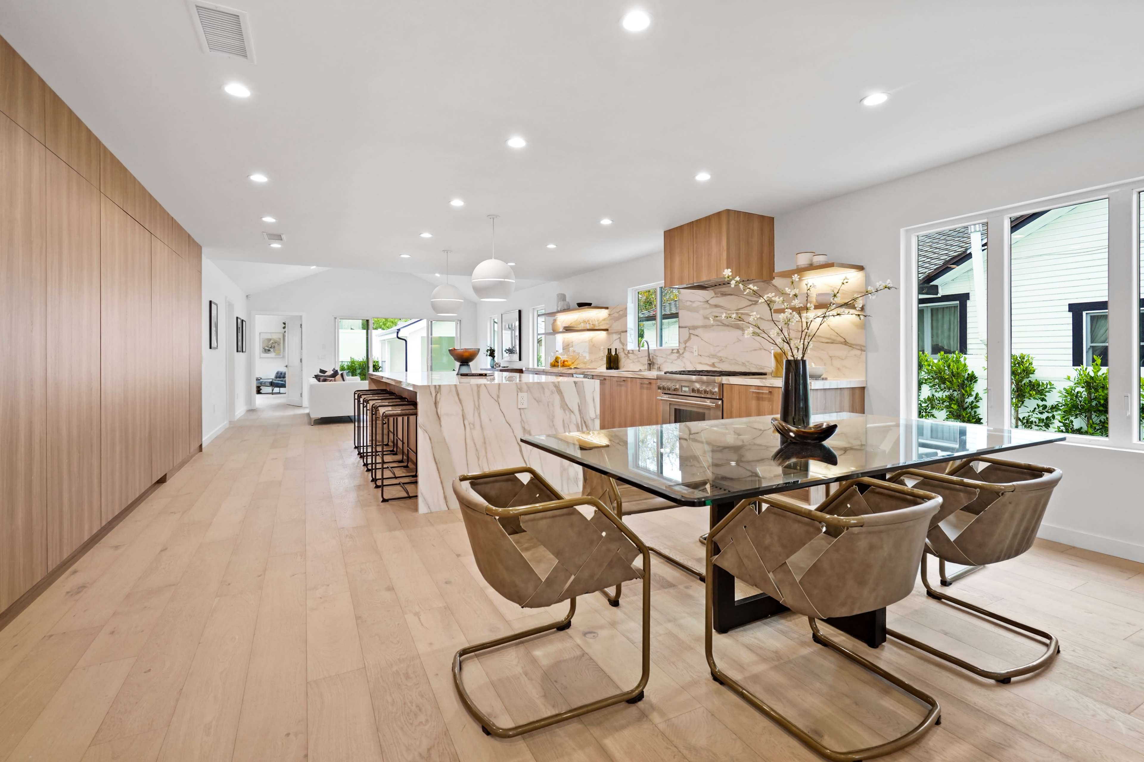 A modern kitchen and dining area features a marble island, sleek cabinetry, and a glass dining table surrounded by upholstered chairs.