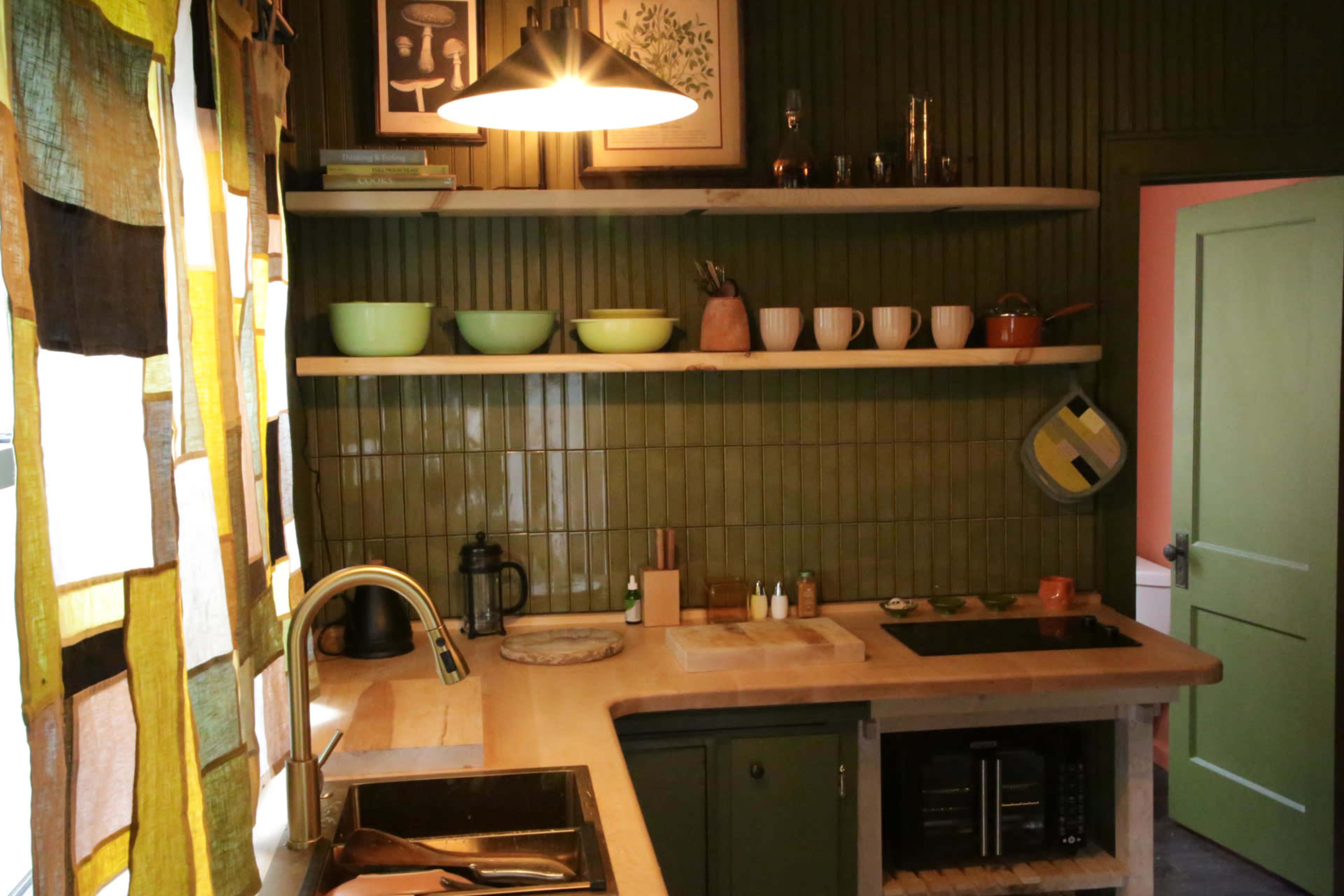 The image shows a kitchen with green walls, wooden shelves, and a countertop featuring various kitchenware arranged neatly.