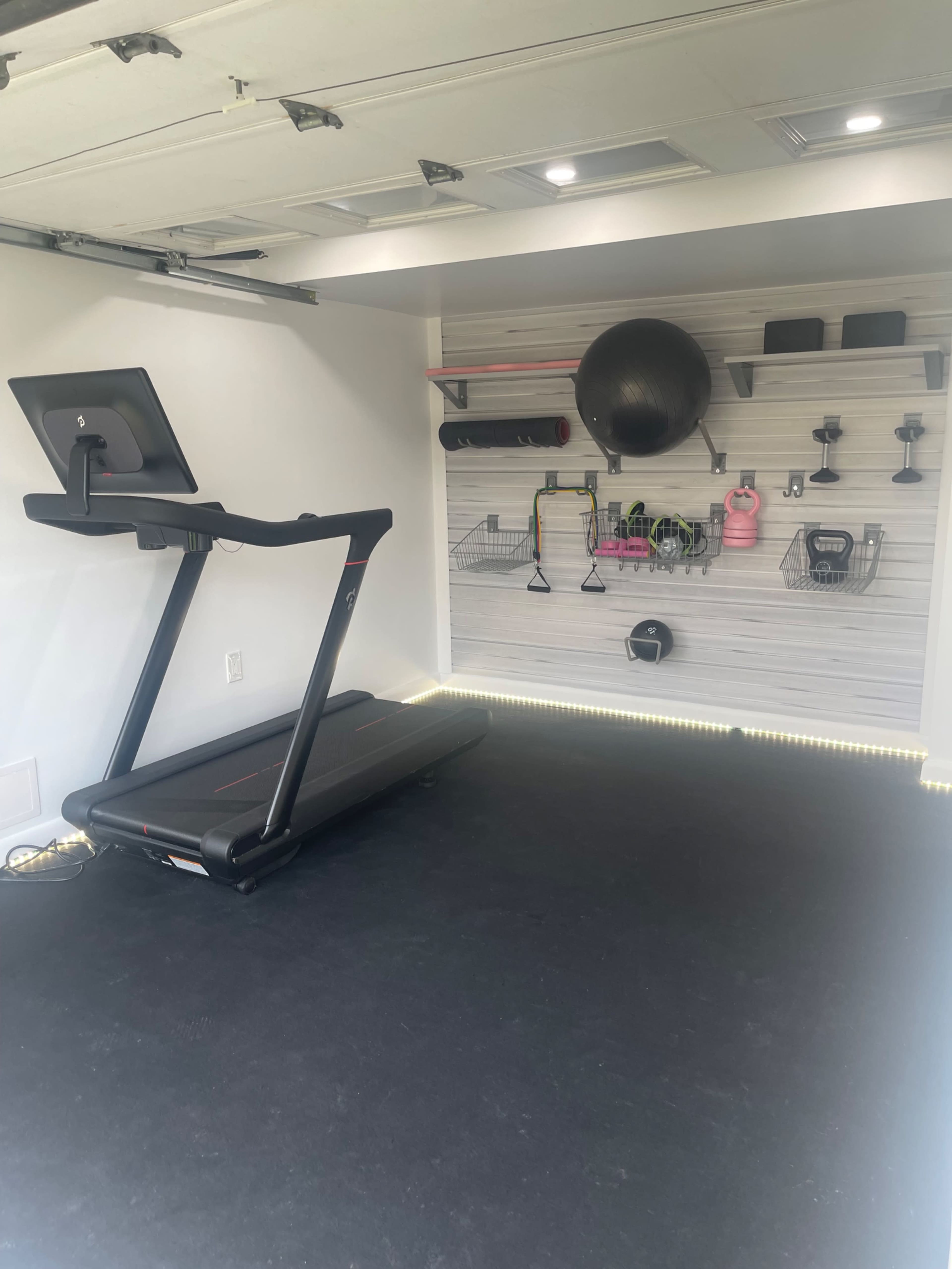 A home gym with a treadmill and various fitness equipment organized on a wall-mounted shelf.