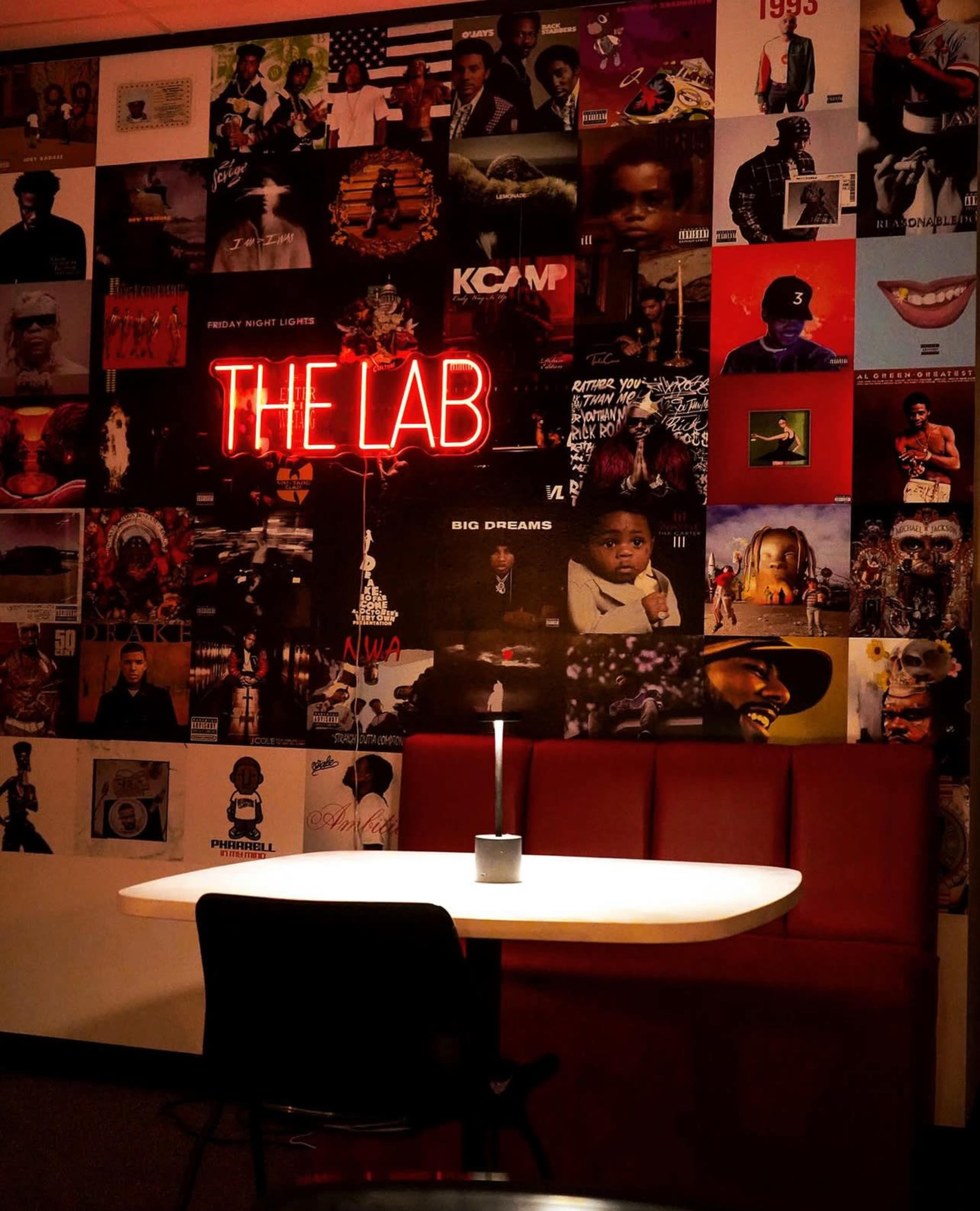 The scene features a dimly lit room with a table and chair in front of a wall covered with various album covers and a neon sign that reads "THE LAB."