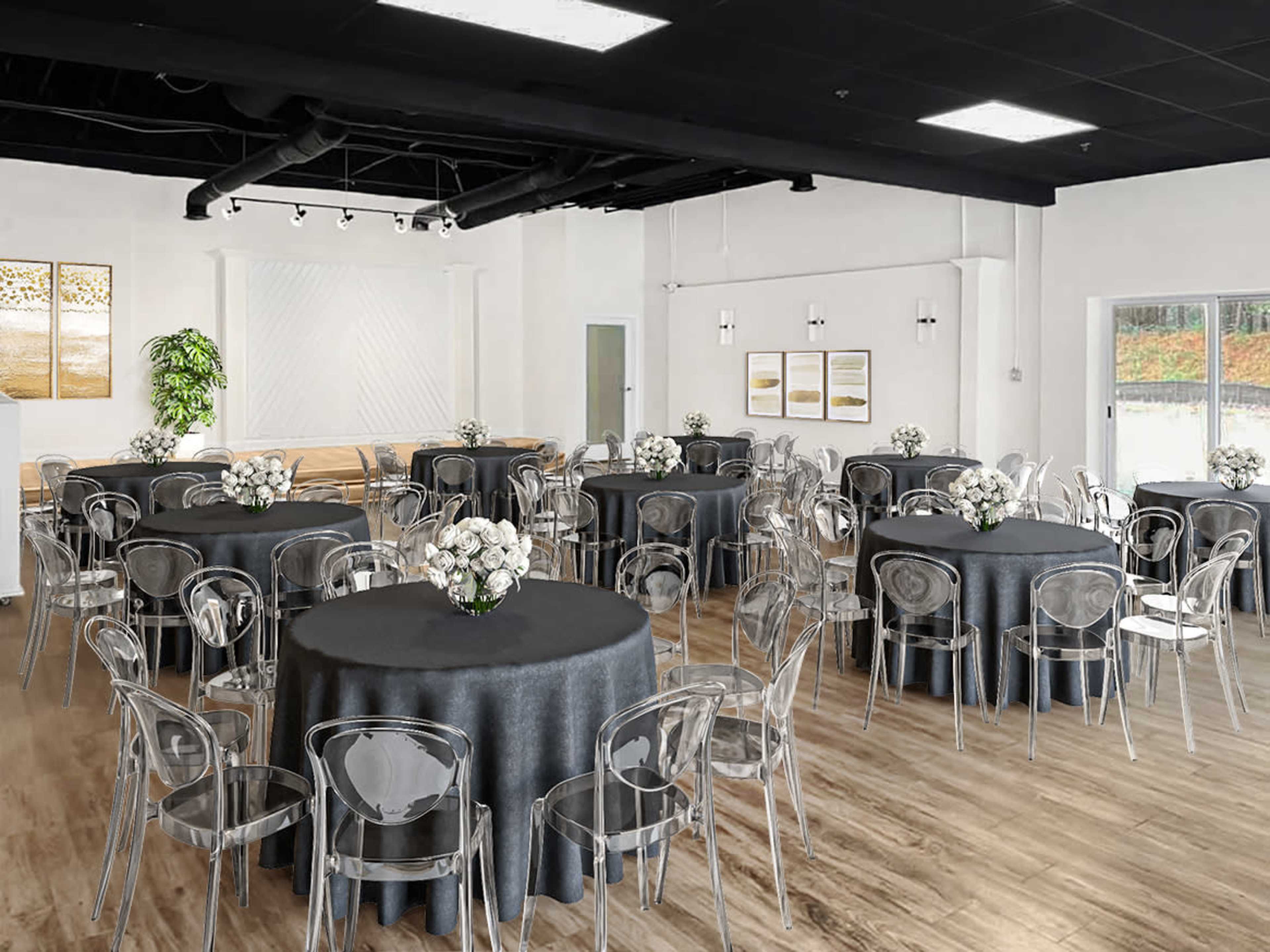 A banquet hall features several round tables covered with dark tablecloths and clear chairs, arranged for an event.