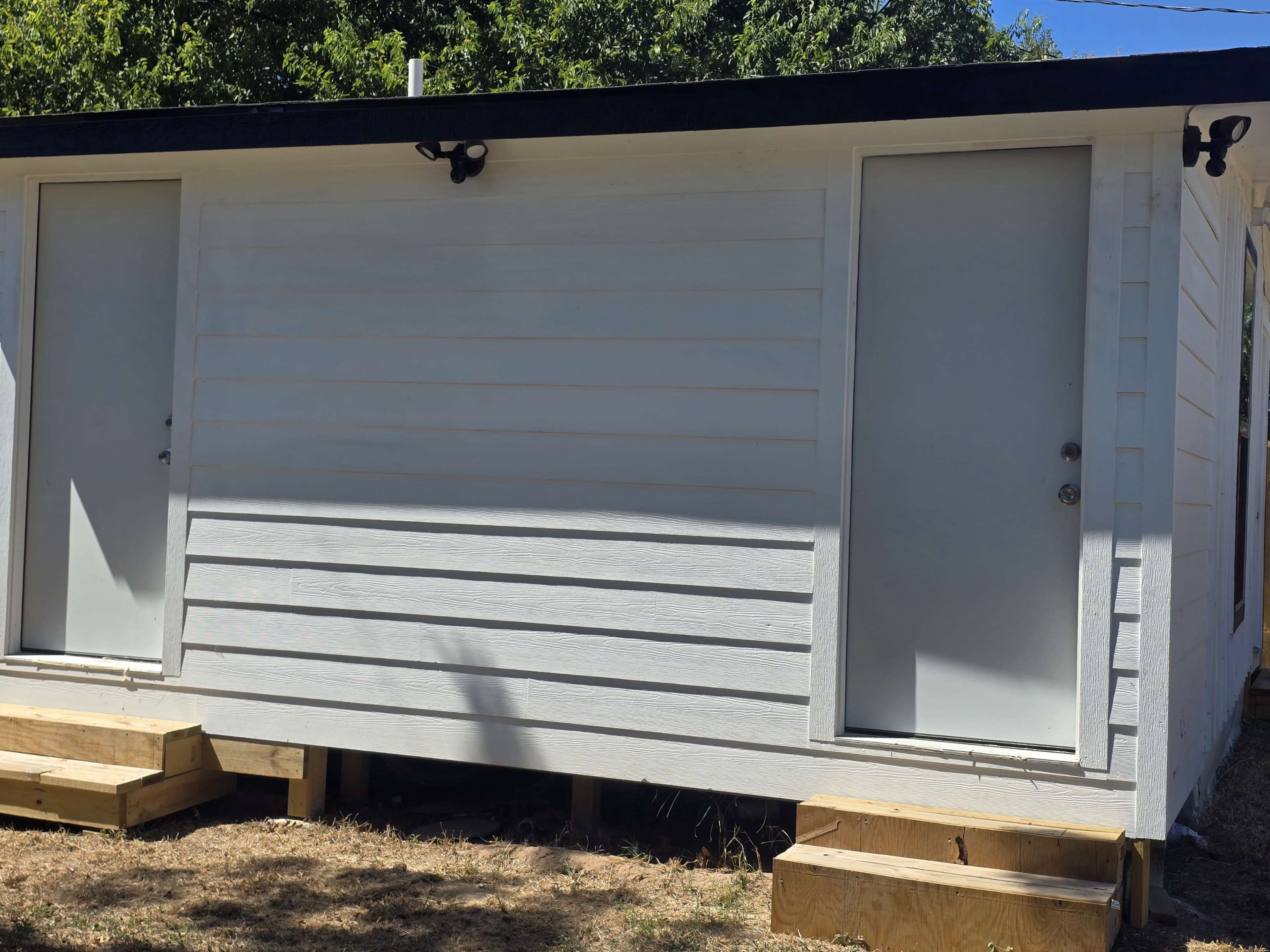 The image shows a small, elevated building with two white doors and a wooden base.