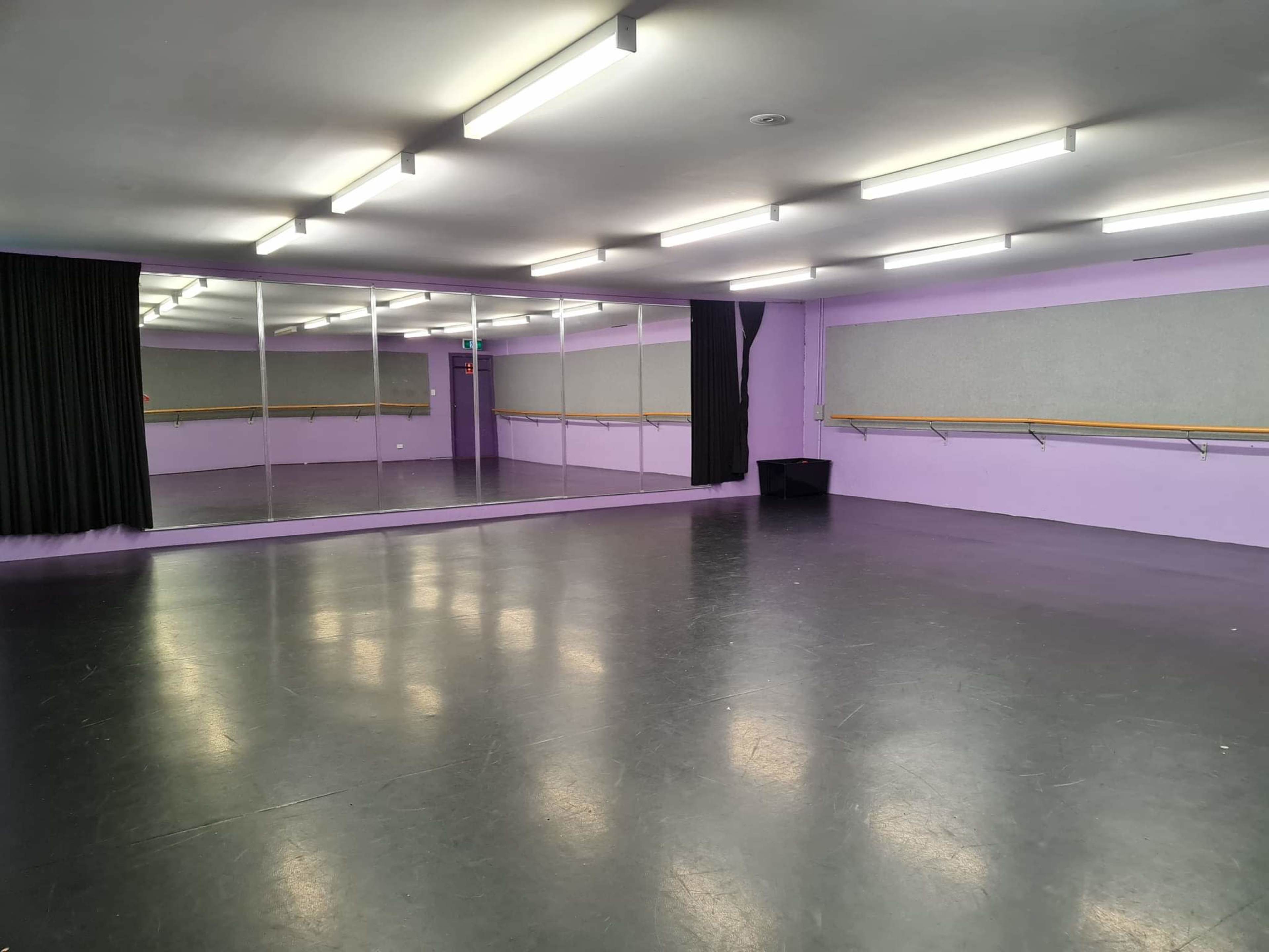 A dance studio with gray flooring, purple walls, and mirrors along one side.