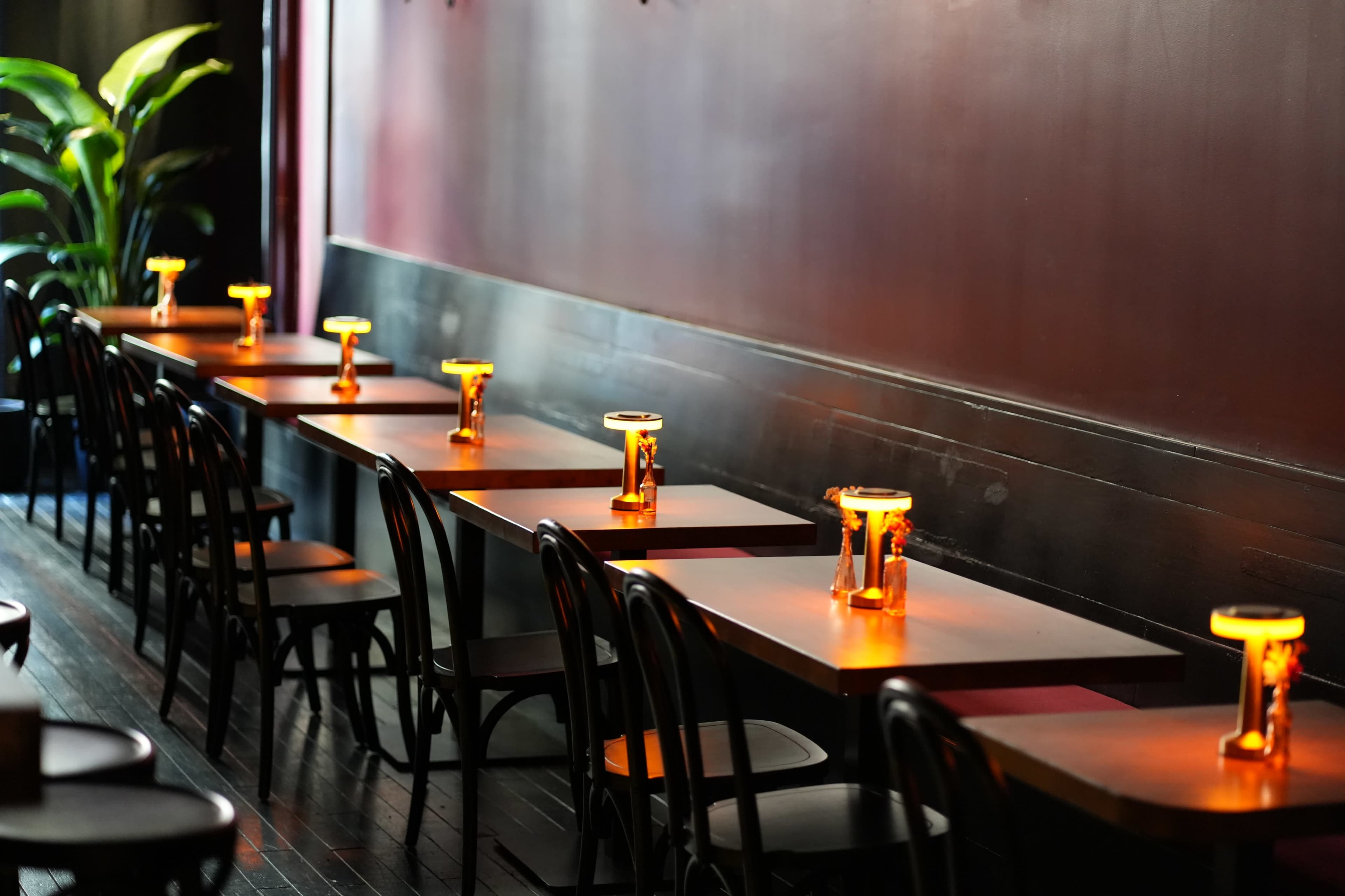 The image shows a row of tables in a dimly lit restaurant, each with a glowing candle centerpiece and black chairs lined against a dark wall.
