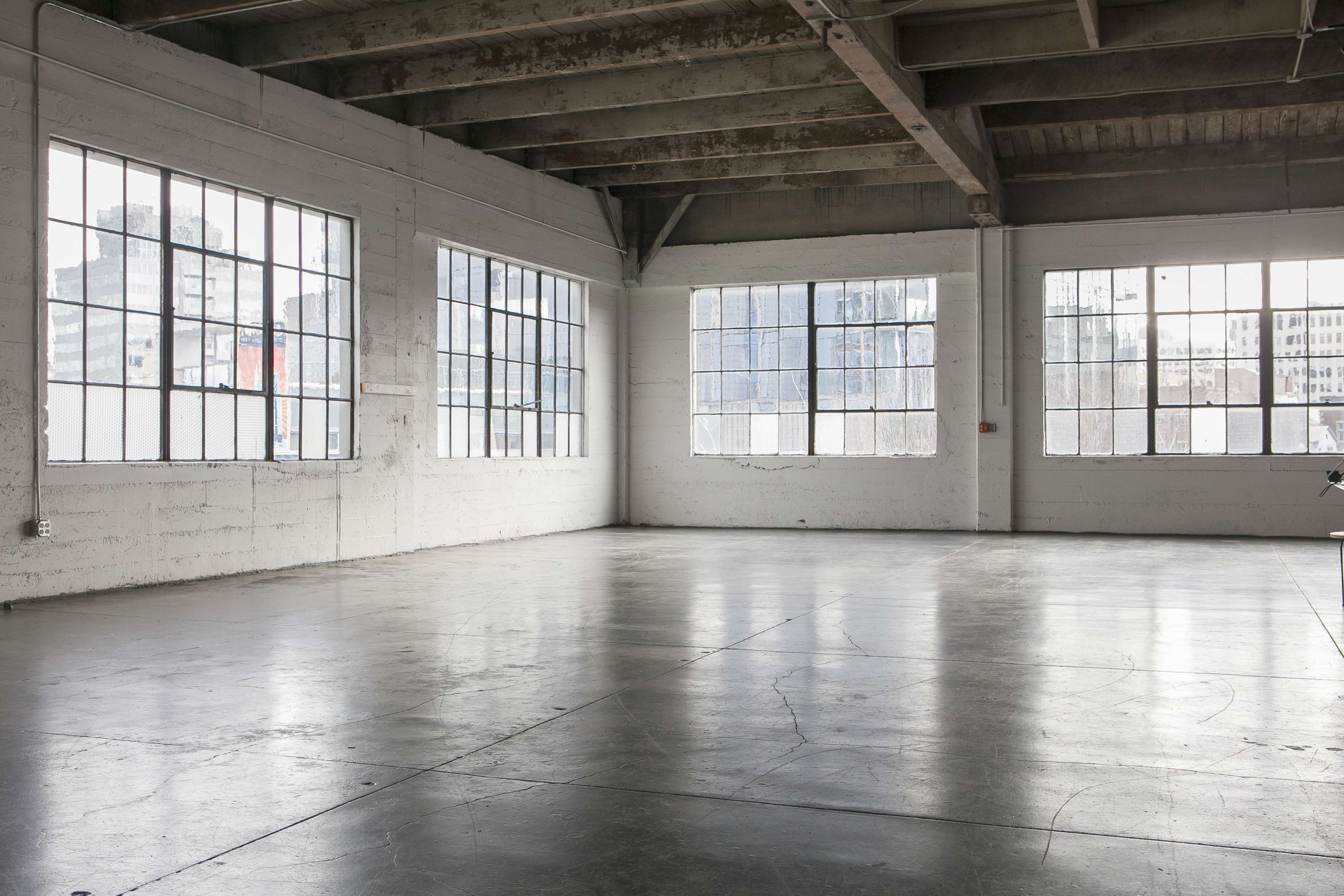 The image shows a spacious, empty industrial room with large windows allowing natural light to enter.