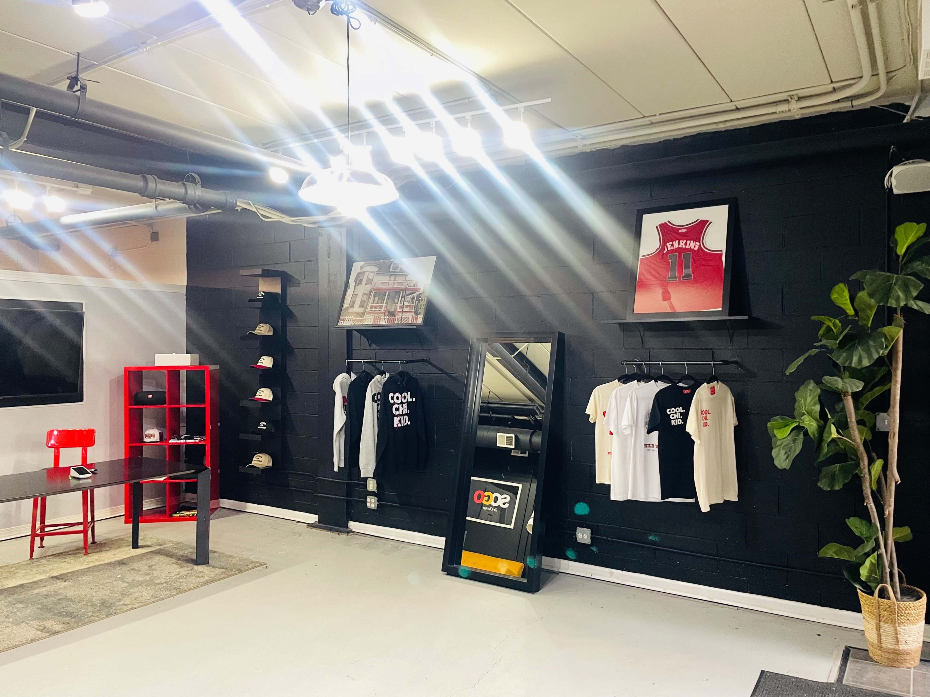 A modern retail space with a black wall displaying clothing and a framed basketball jersey, illuminated by overhead lights.