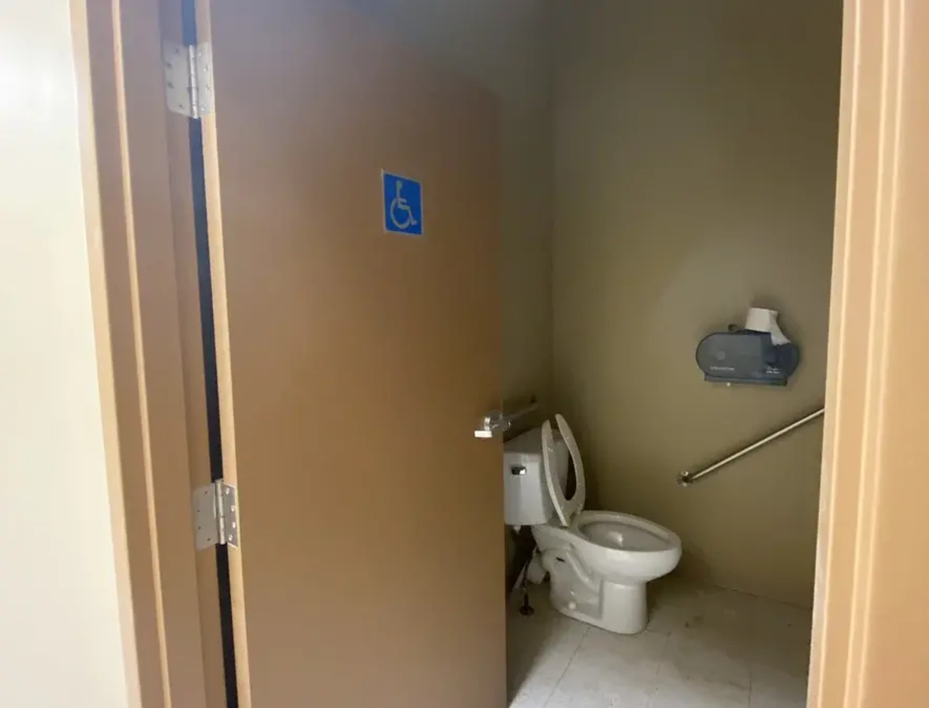 A partially open door to a single restroom, featuring a toilet and an accessible sign.