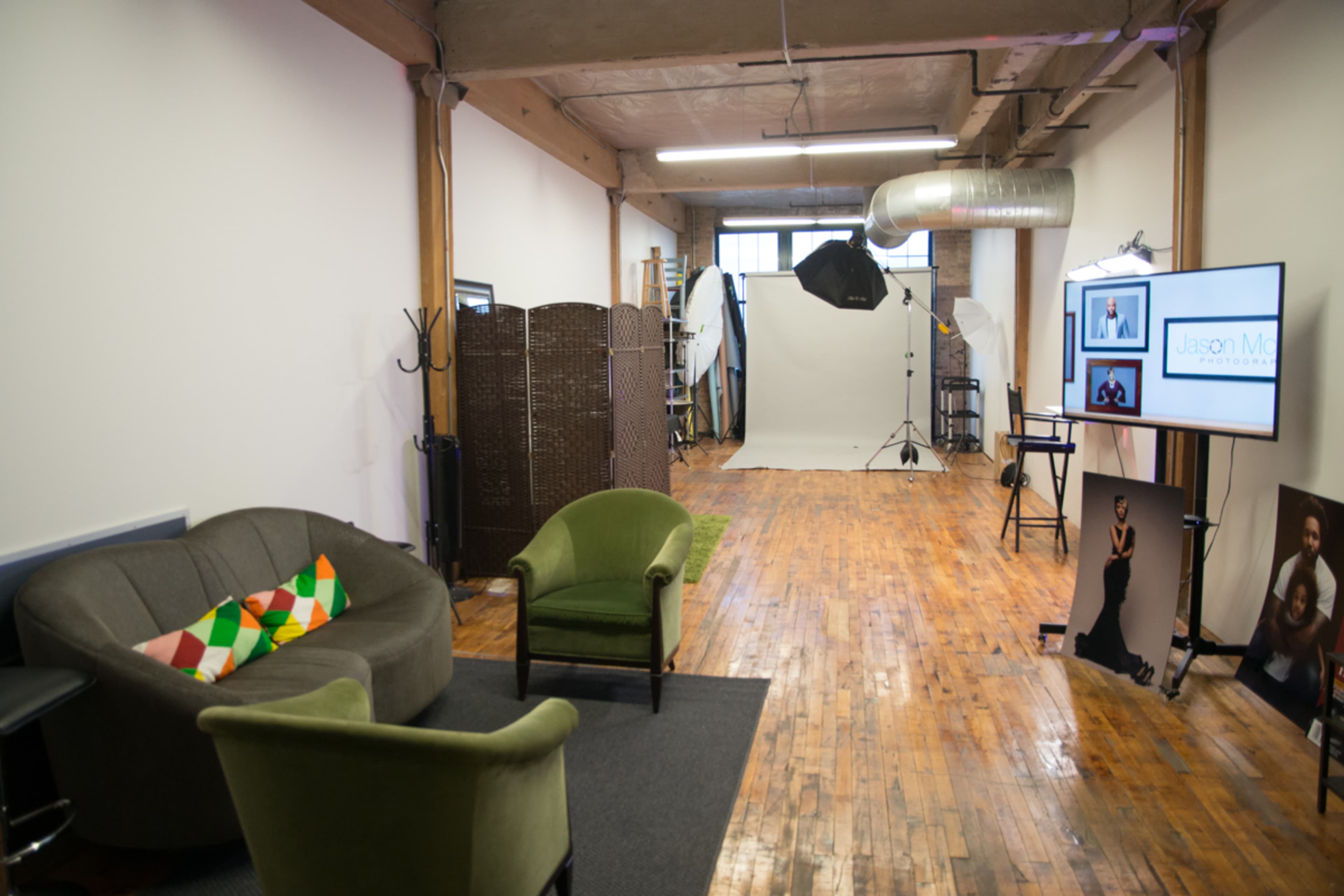 The image shows a spacious, well-lit studio featuring seating arrangements, a backdrop setup for photography, and a monitor displaying content.