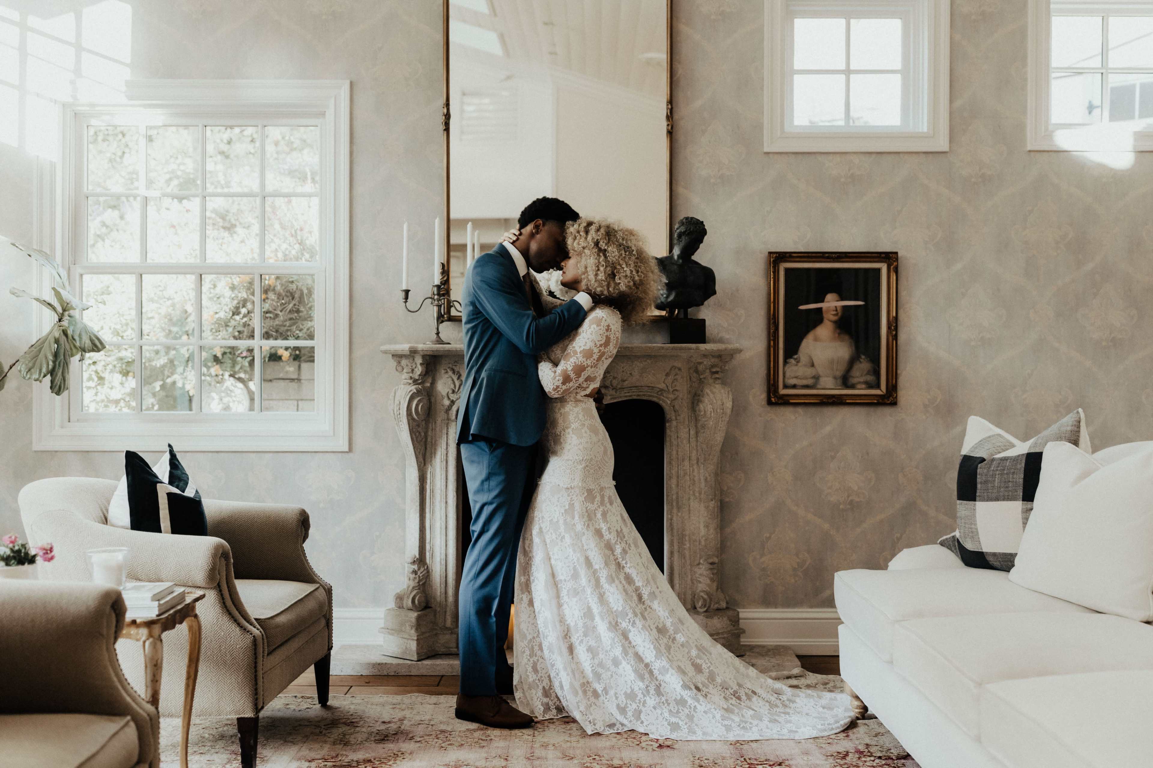 A couple embraces in a stylish living room with a fireplace and large windows.