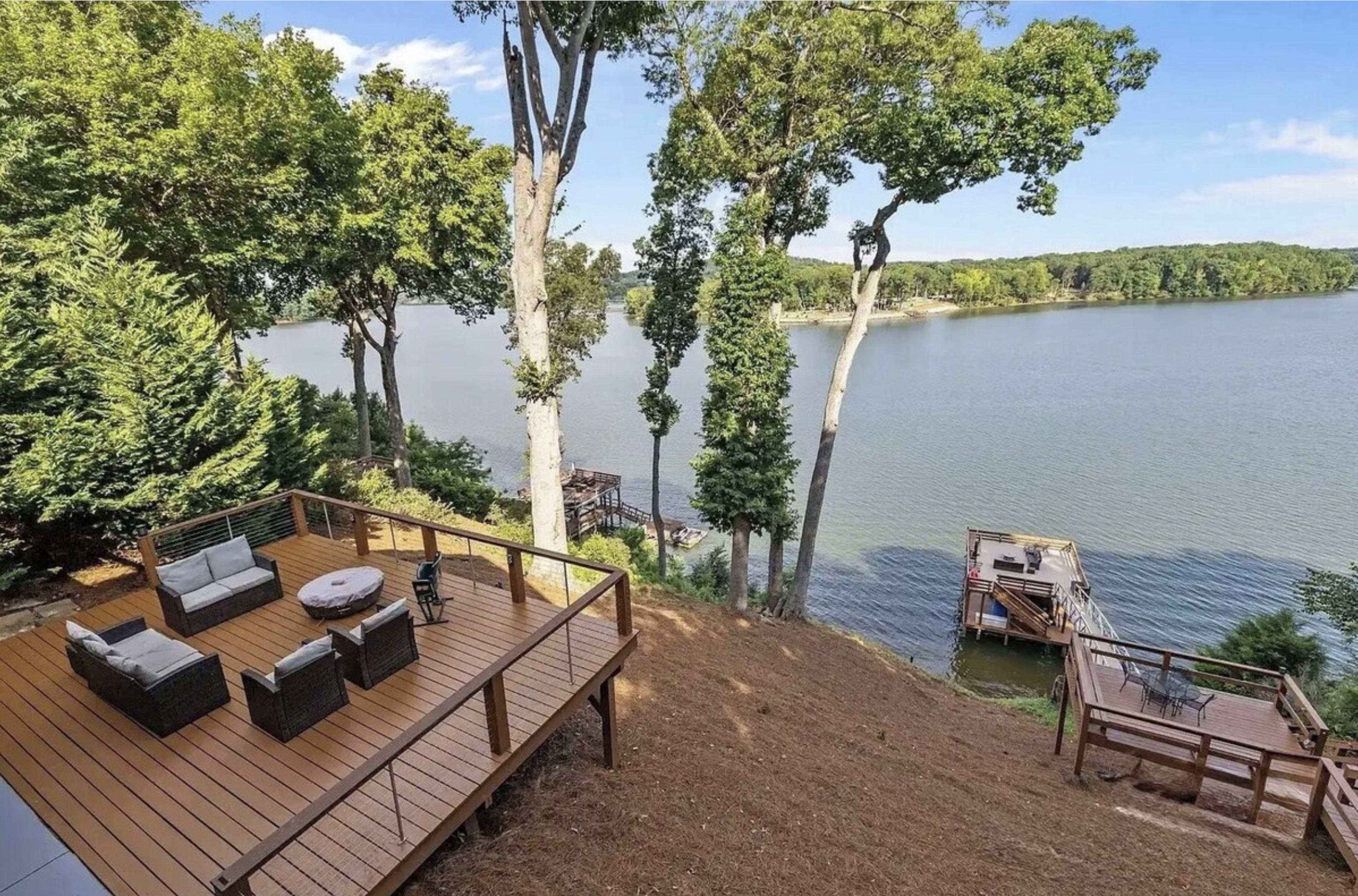 The image shows a wooden deck overlooking a lake, with a seating area and a dock visible in the background.