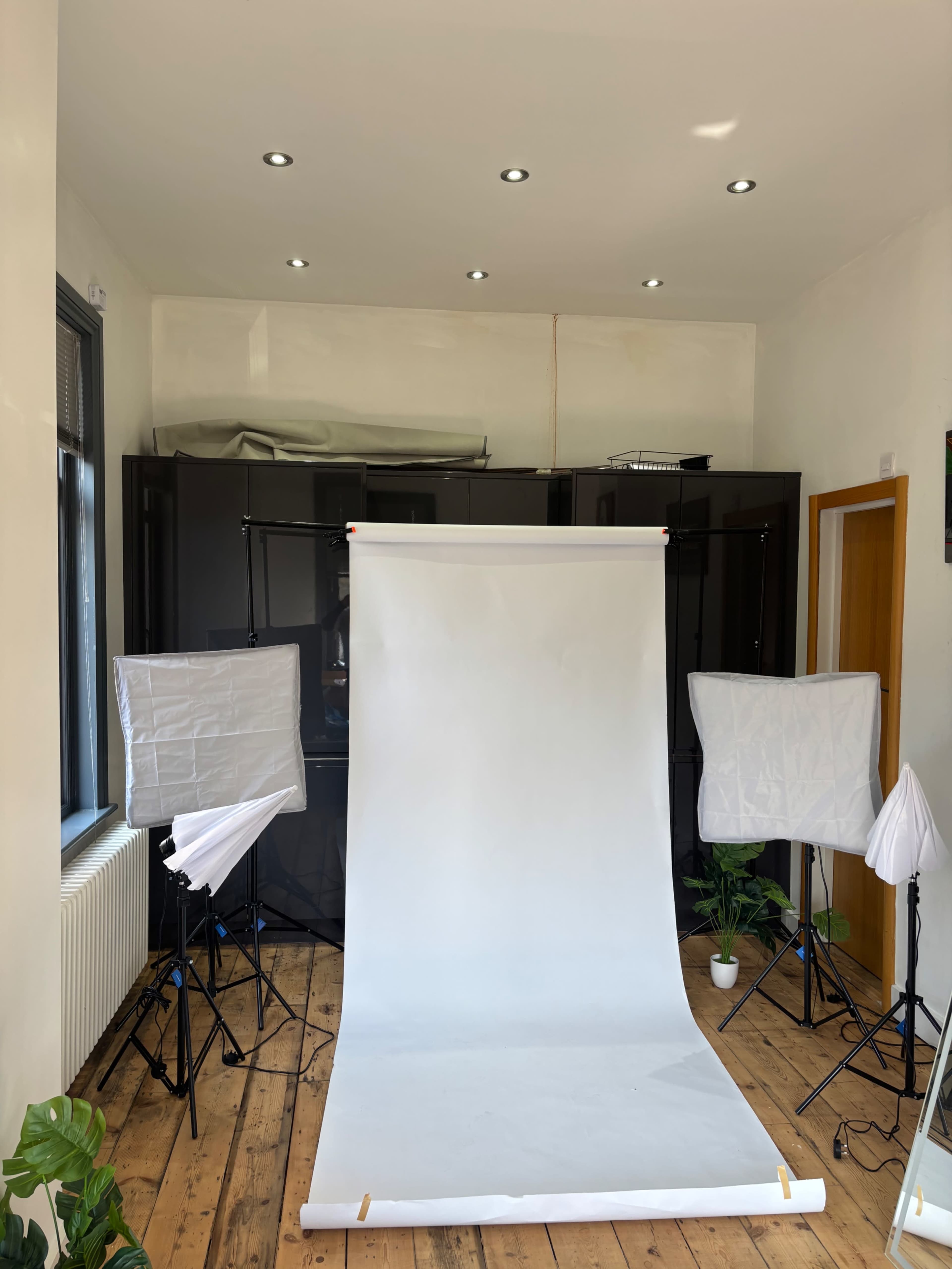The image depicts a well-lit photo studio with a smooth white backdrop and multiple lights on stands arranged around it.