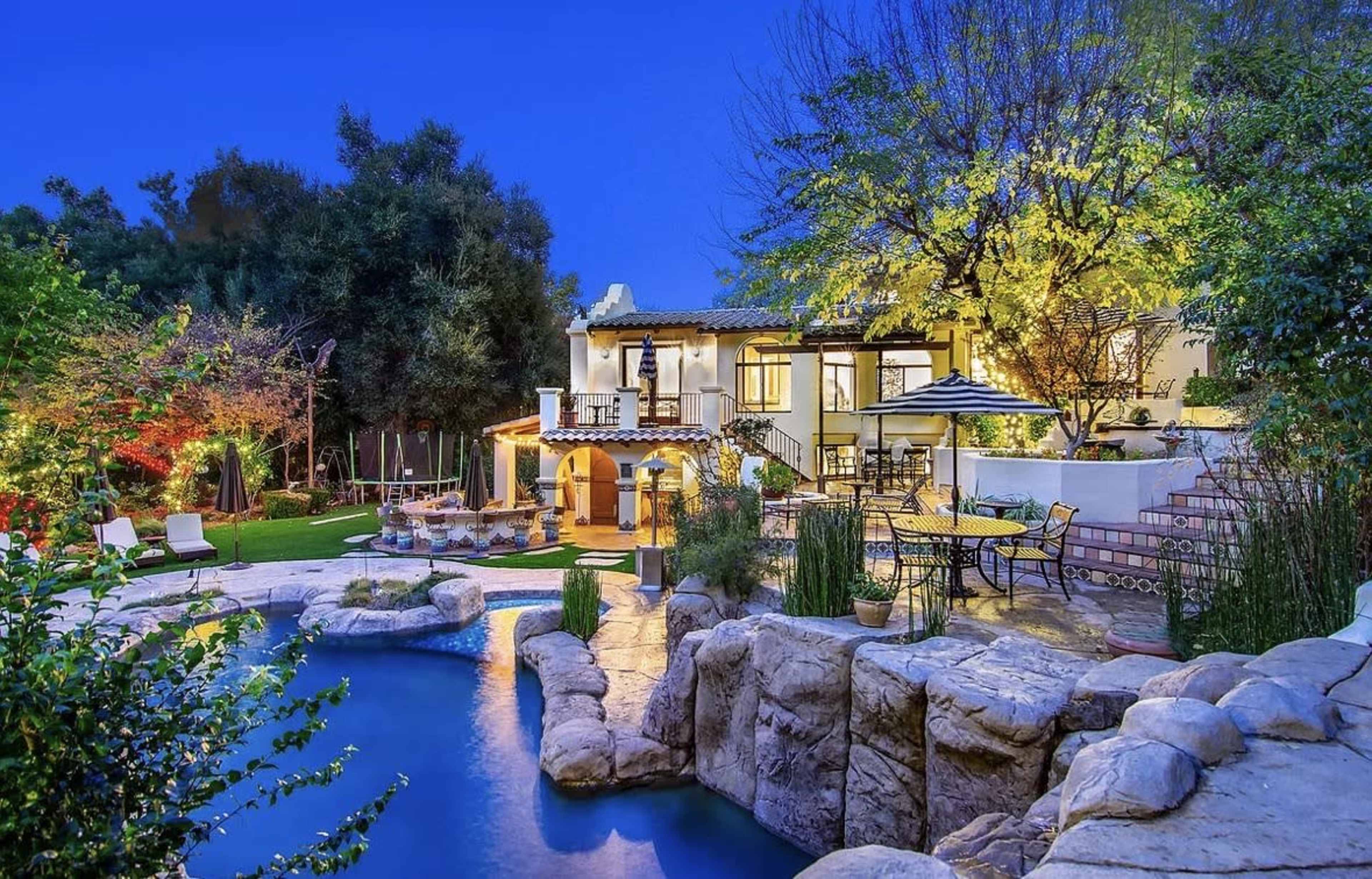 A spacious house with a landscaped garden, swimming pool, and outdoor seating illuminates the evening sky.