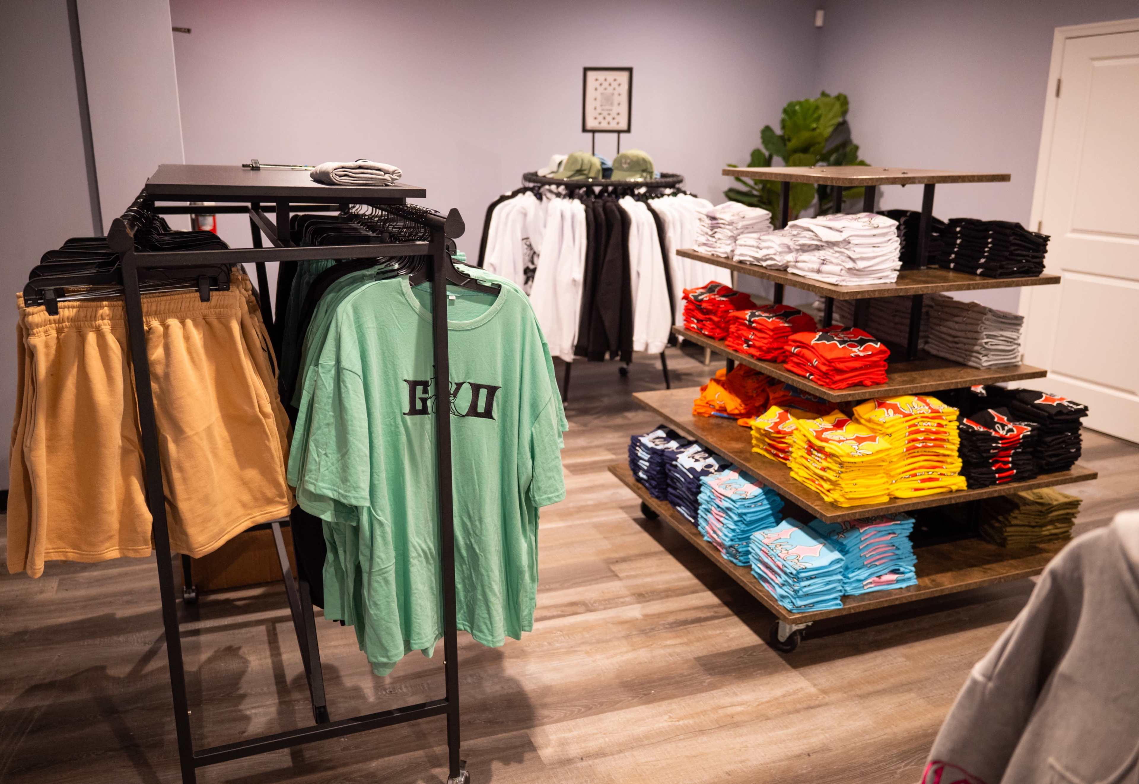 A retail space features racks of clothing, including t-shirts and shorts, organized on tables and hangers.