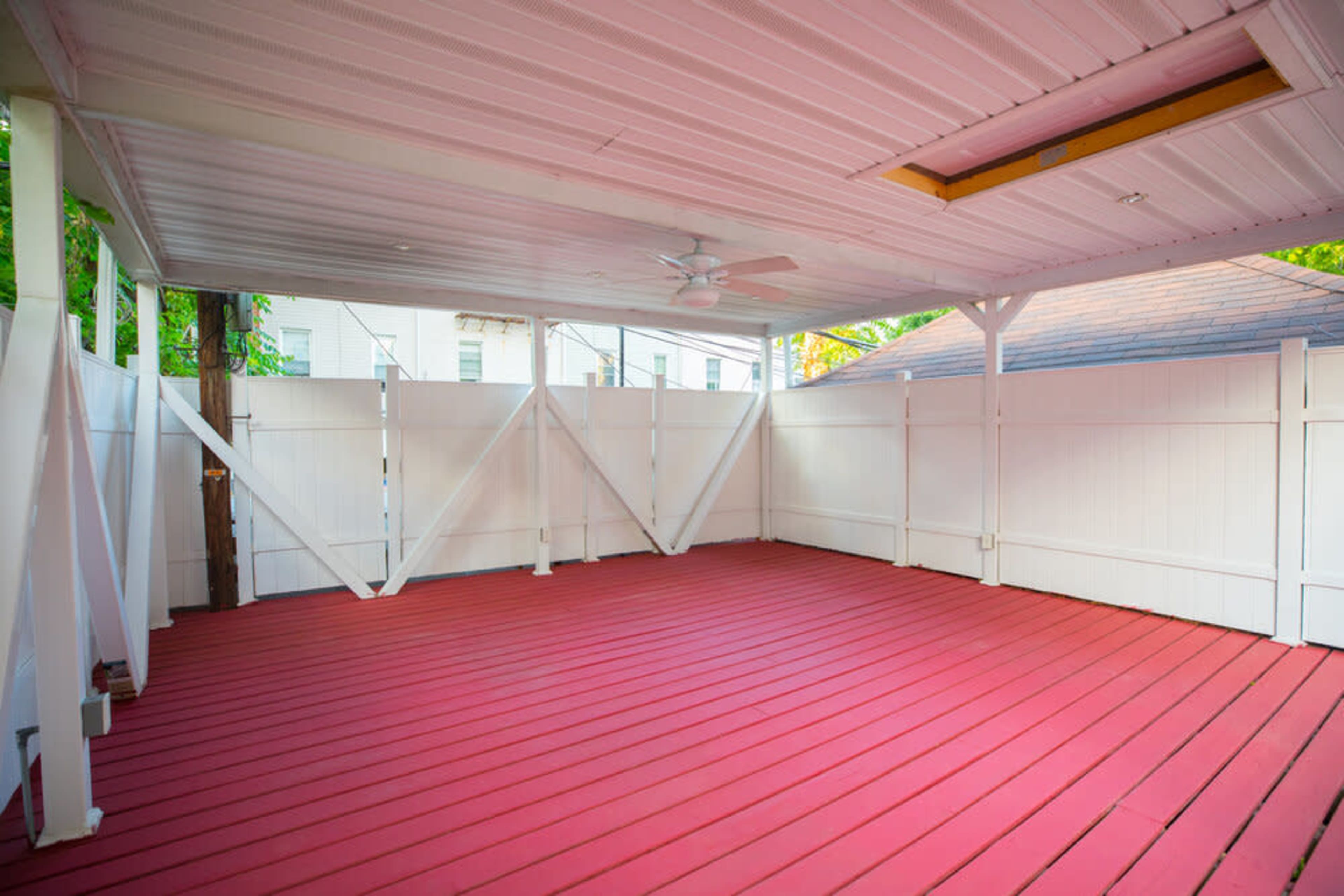 A spacious, covered deck area with red wooden flooring and white fence panels.