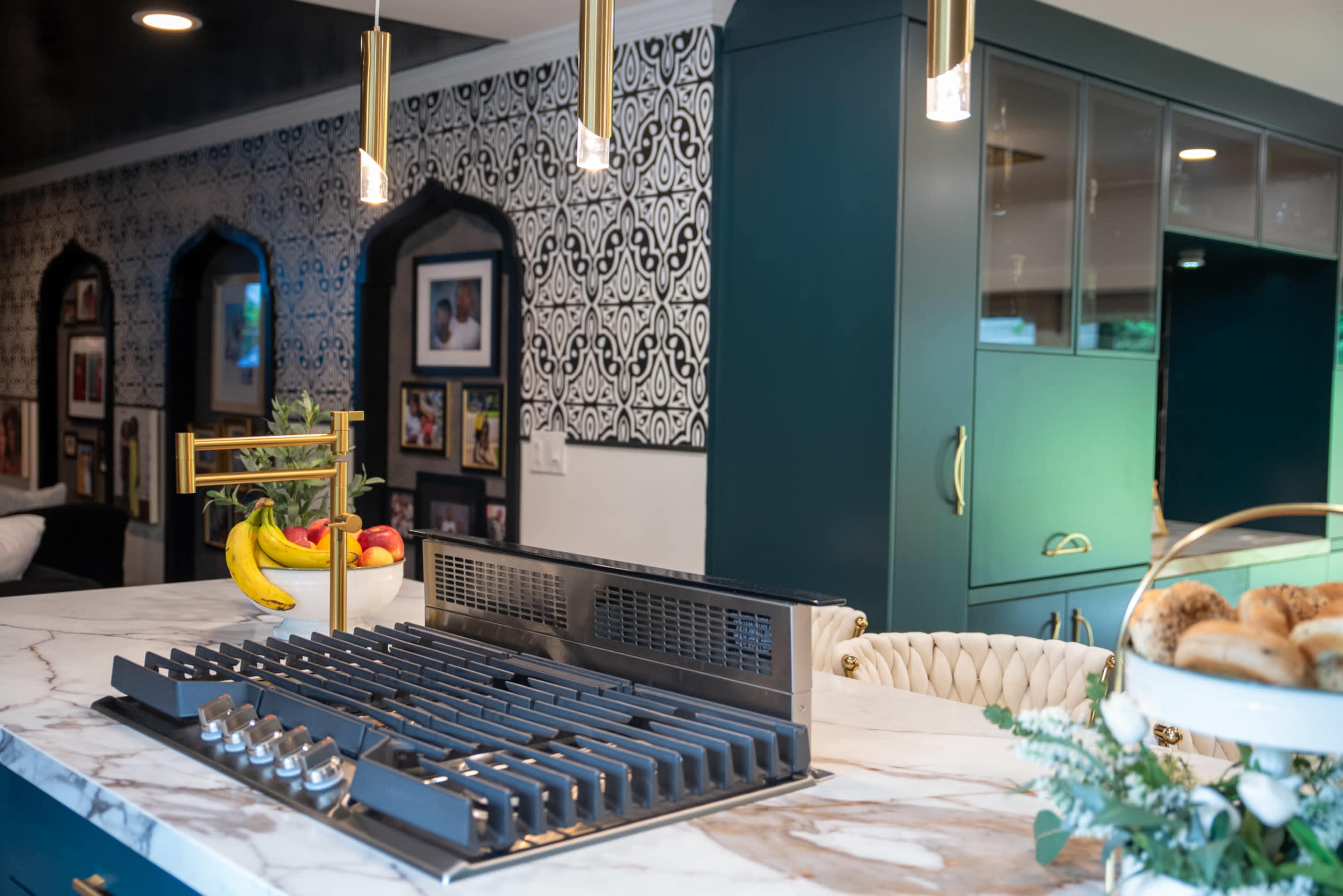 The image features a modern kitchen with a large marble island, a gas stove top, vibrant blue cabinetry, and decorative wallpaper with a geometric pattern.