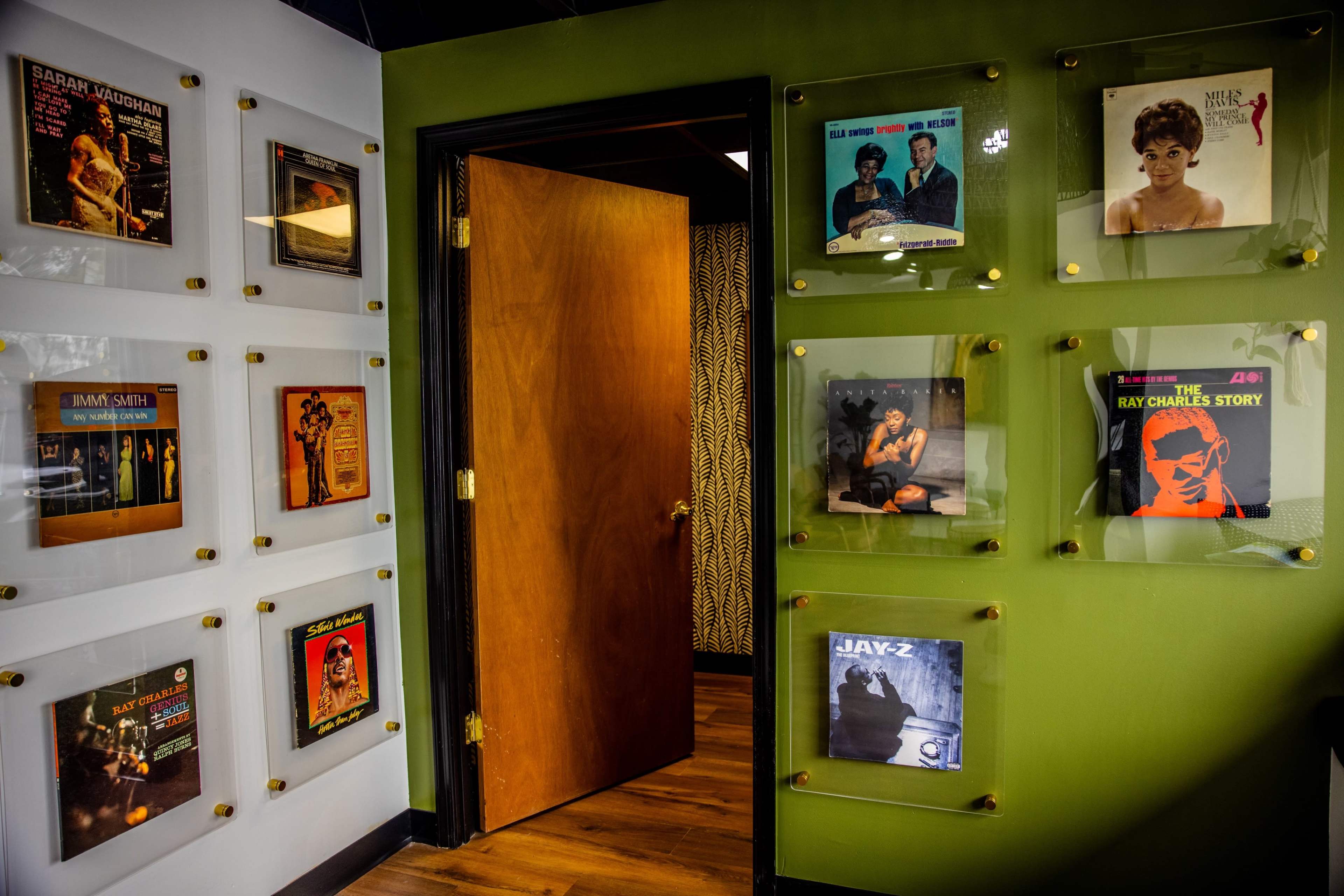 A wall adorned with framed vinyl record covers and a wooden door leading to another room.