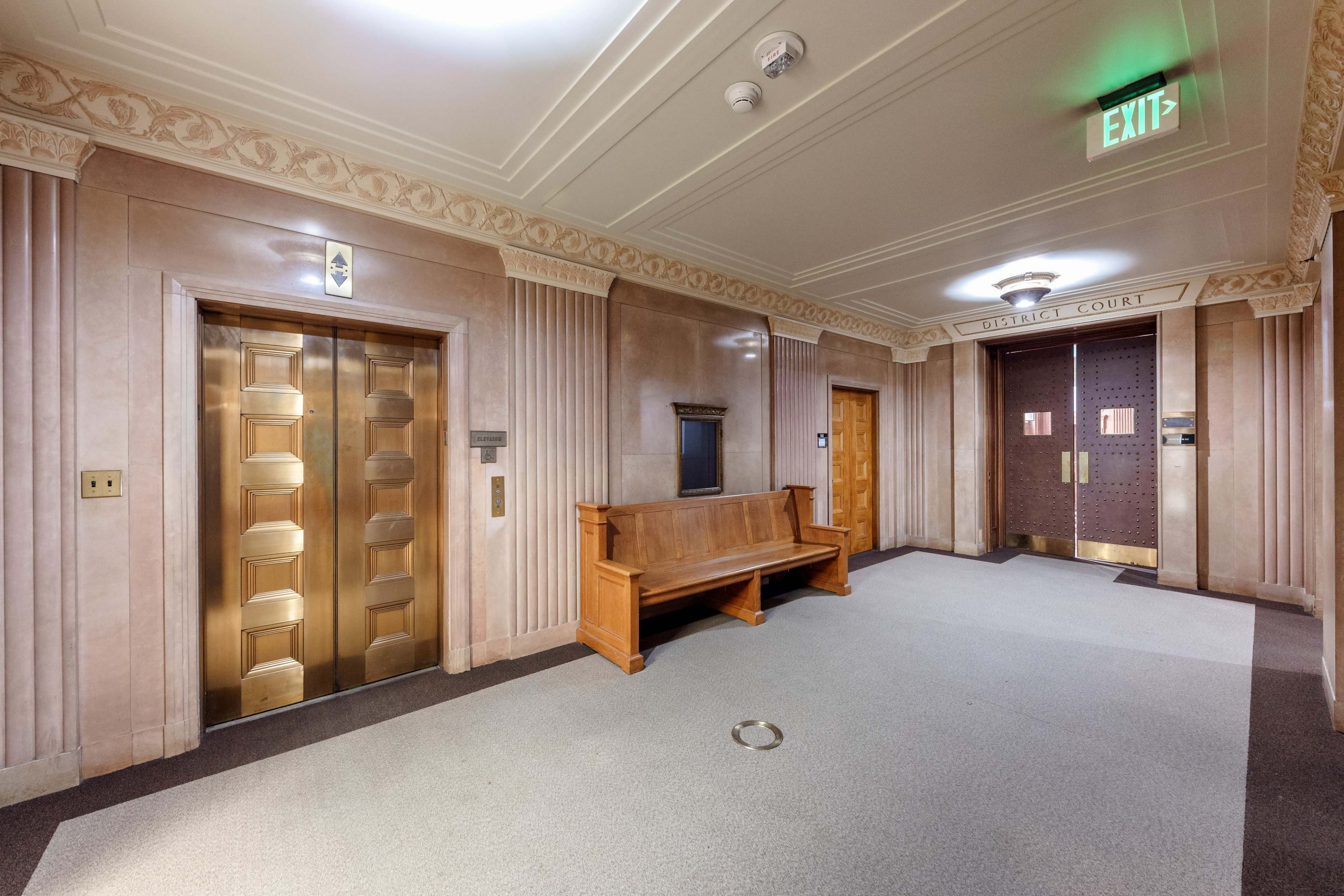 The image shows a corridor with two elevator doors, a wooden bench, and a sign indicating "CIRCUIT COURT" near a set of double doors.