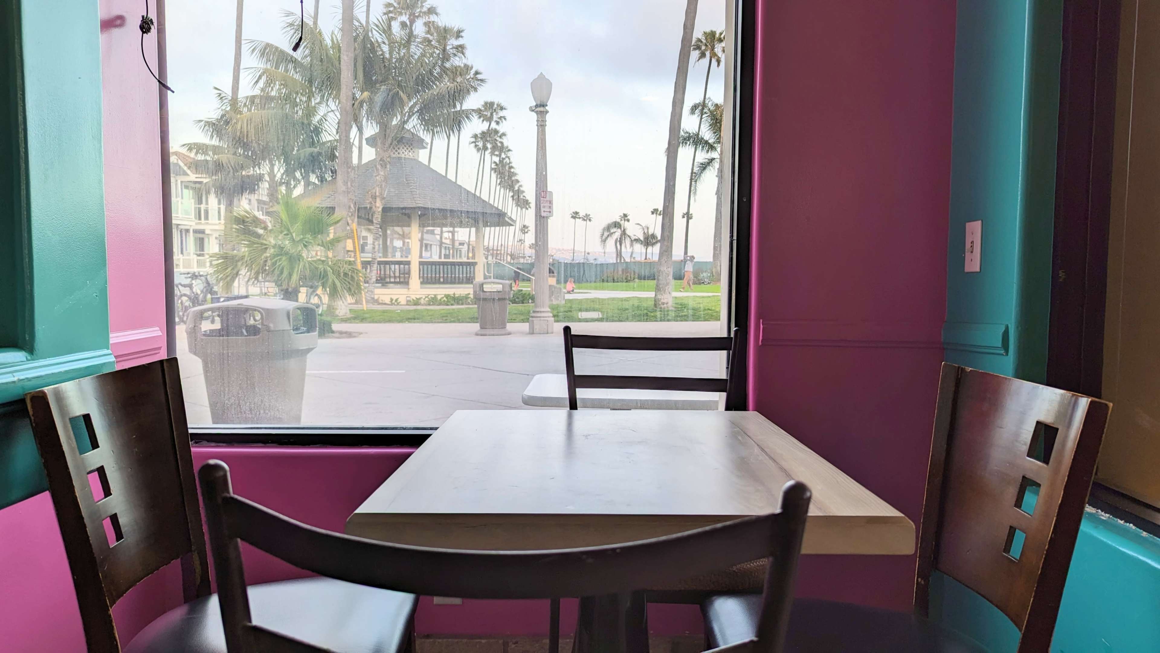 A table and chairs inside a café, with a view of palm trees and a gazebo through a large window.