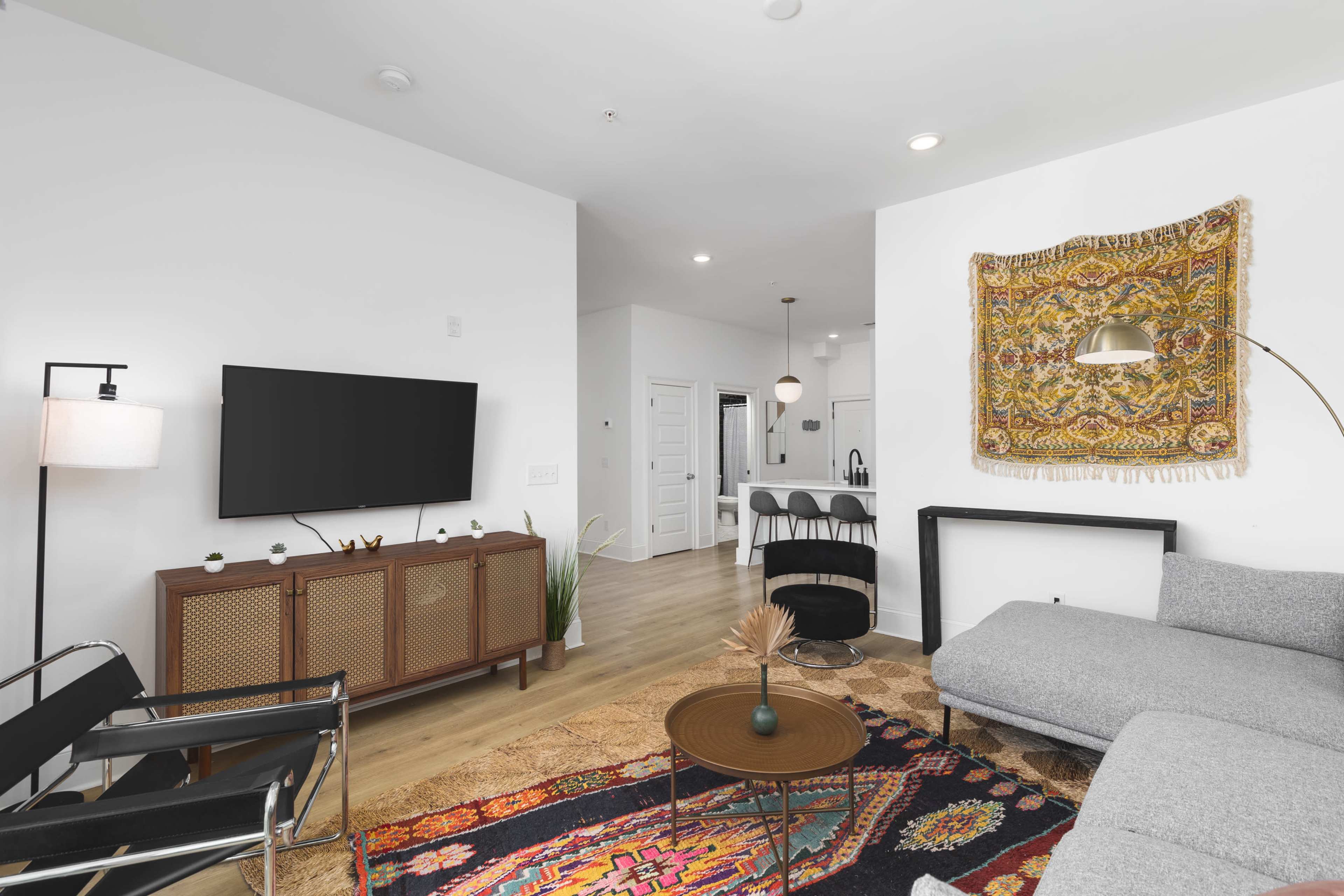 A modern living room with a gray sectional sofa, a wooden TV cabinet, a round coffee table, and a colorful area rug.