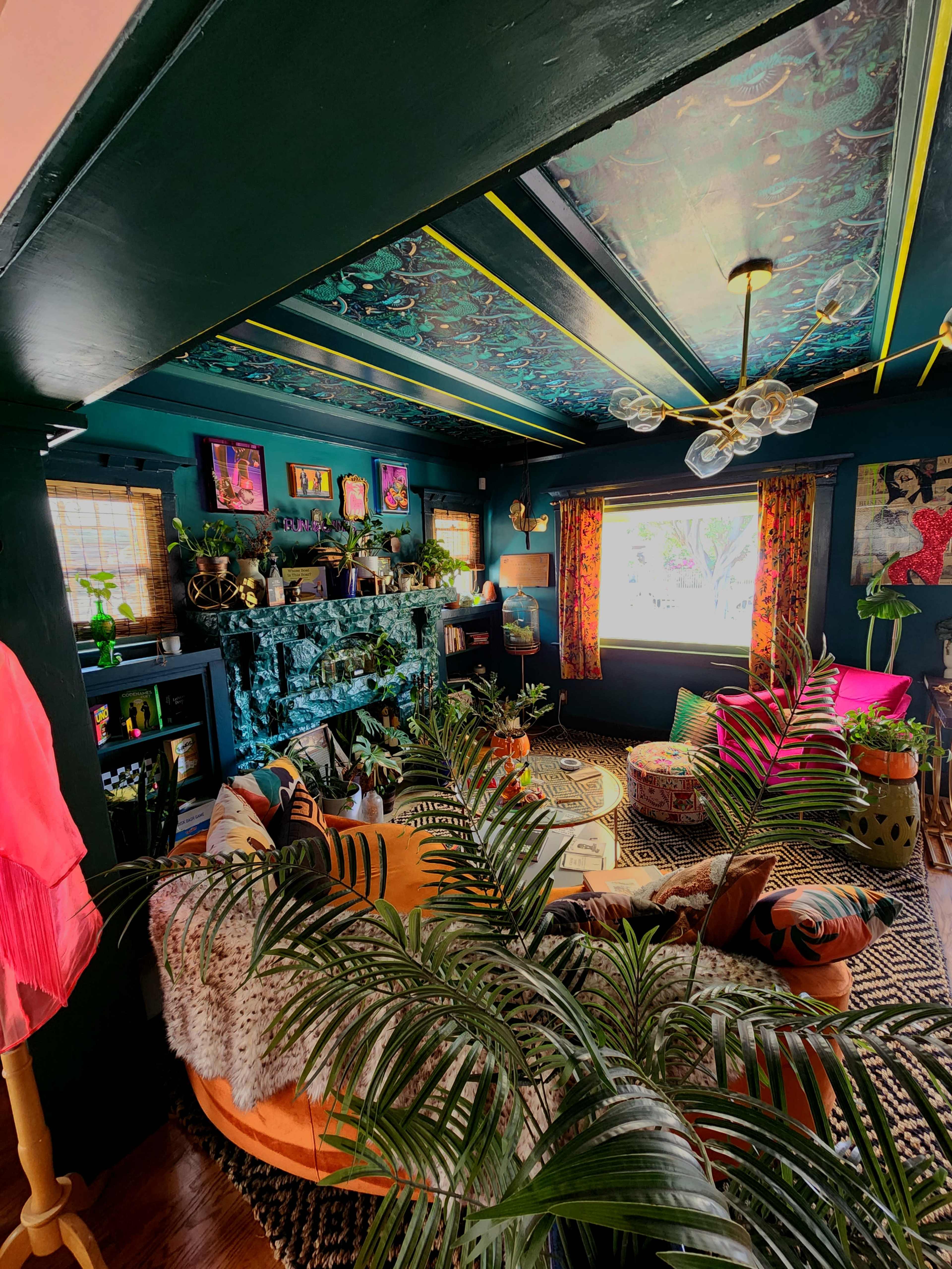 The image shows a vibrant living room filled with plants, colorful furniture, and artistic decorations on the walls.