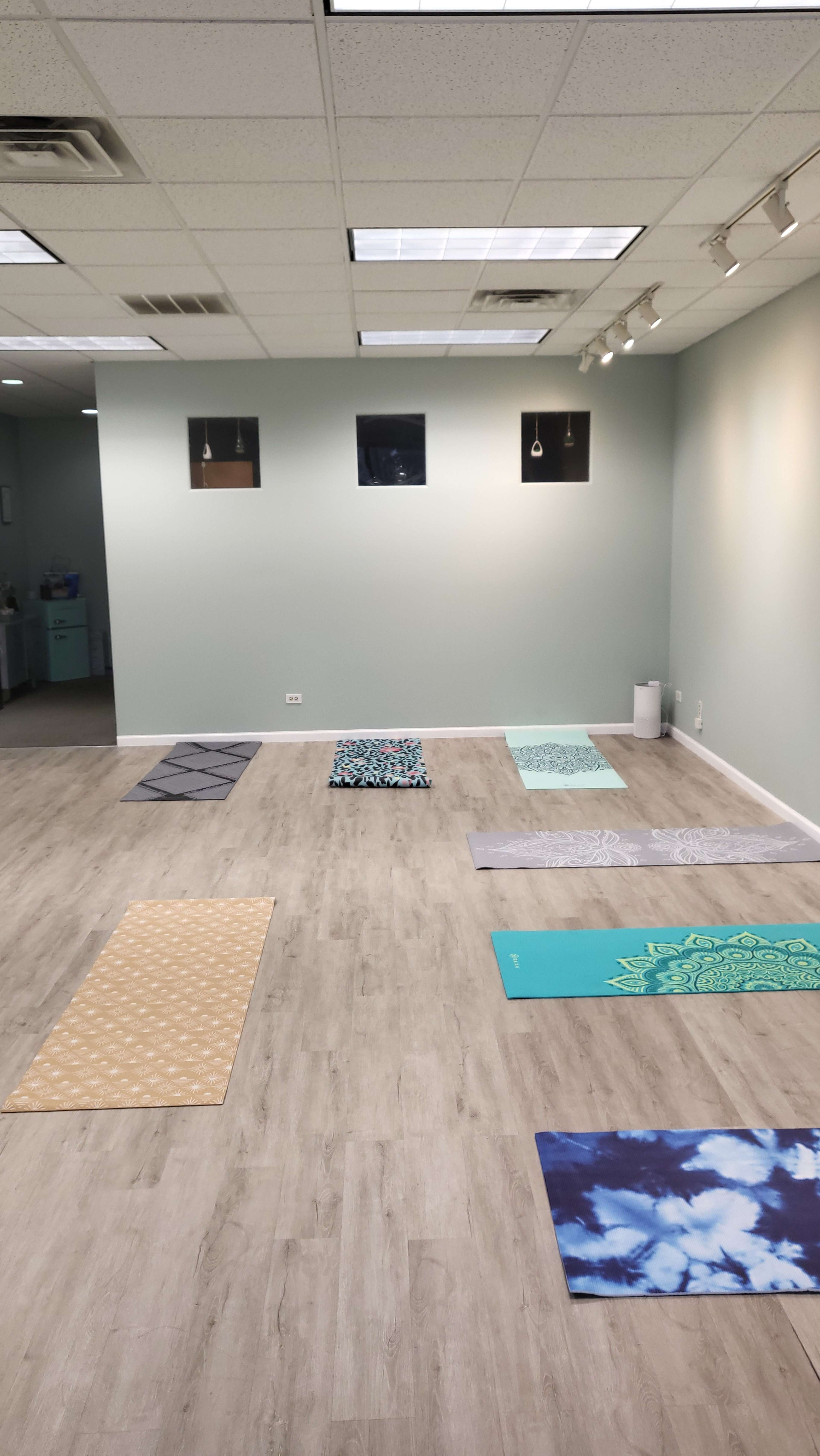 A bright yoga studio with several yoga mats arranged on the wooden floor, set against light green walls.