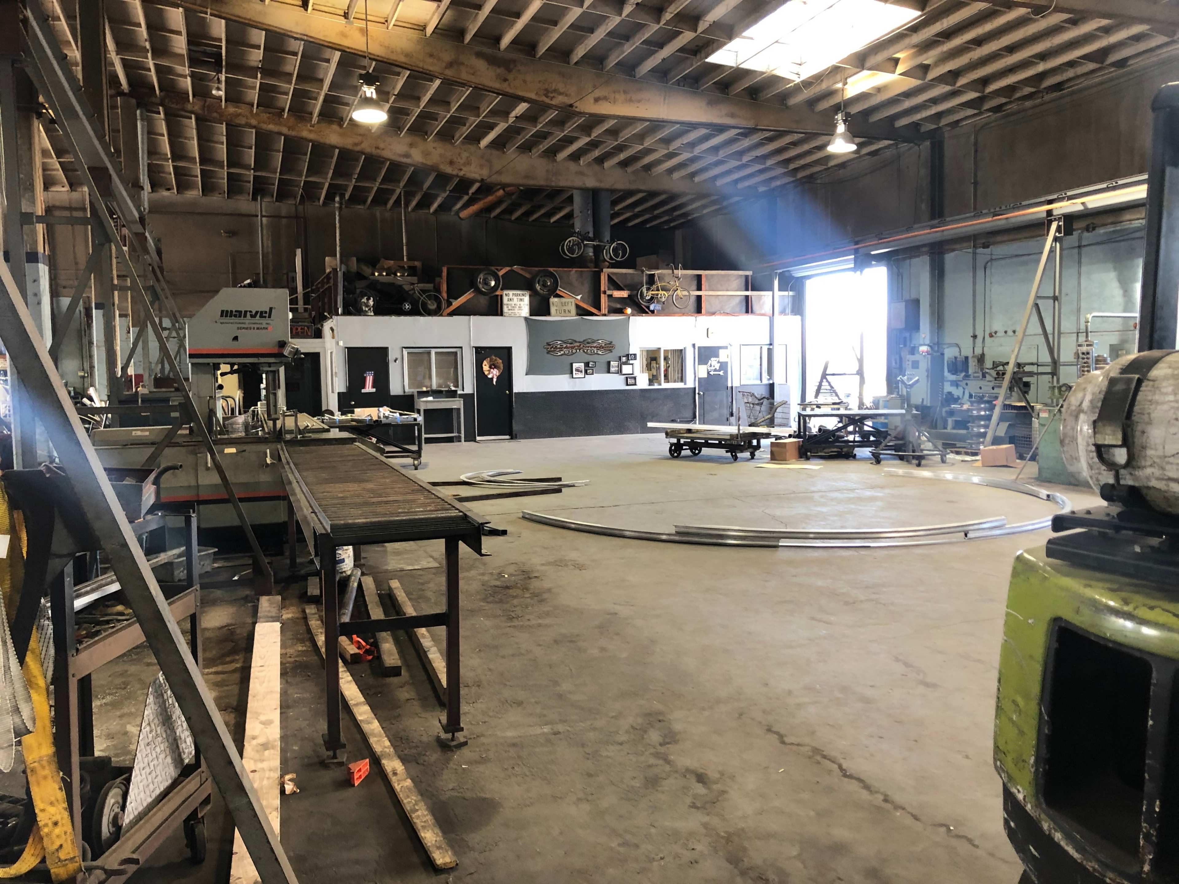 The image shows a large industrial workshop with various tools, equipment, and work areas, including a circular section on the floor.