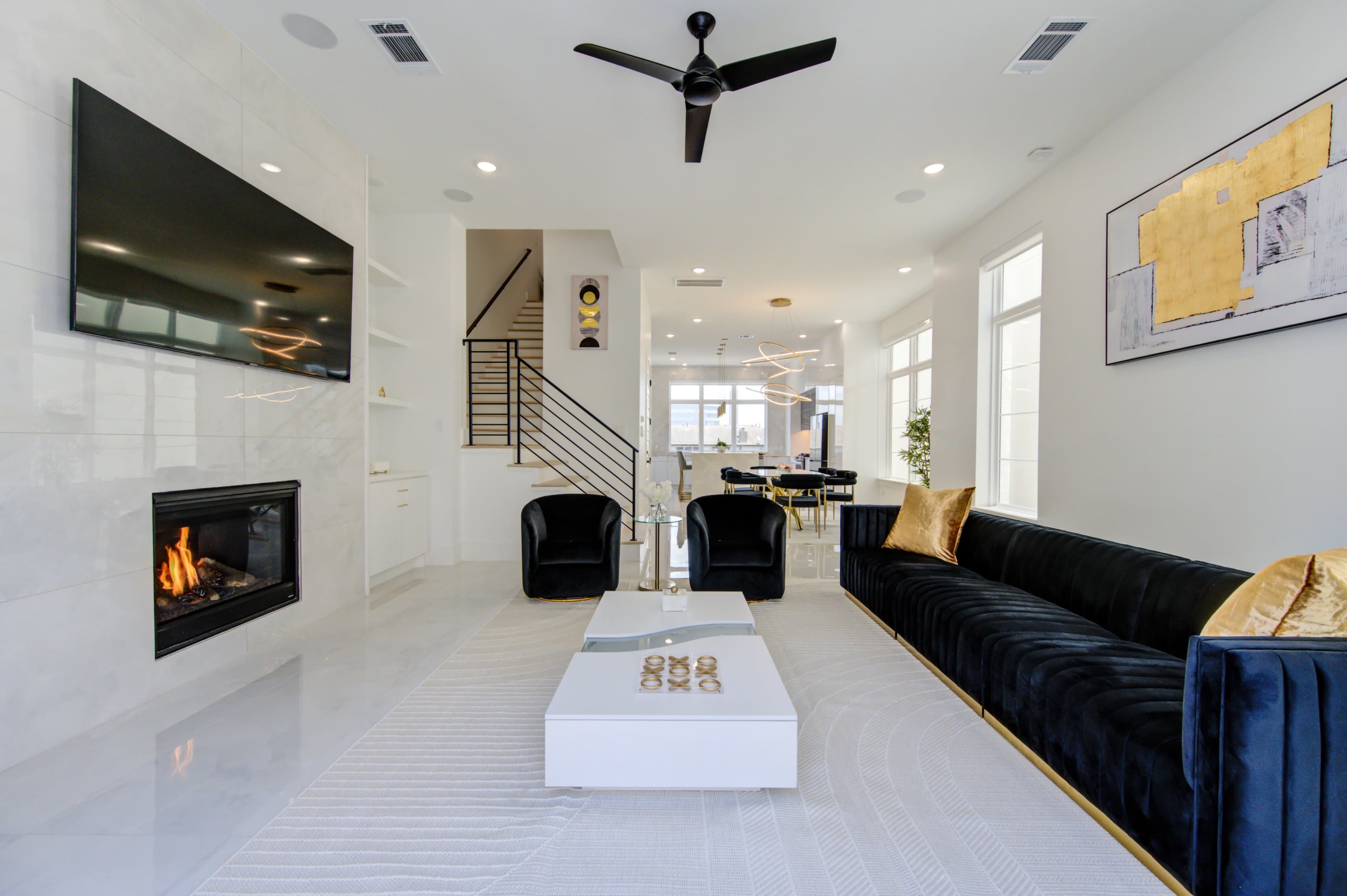 A modern living room with a fireplace, a large television mounted on the wall, a sleek sofa, and a dining area in the background.