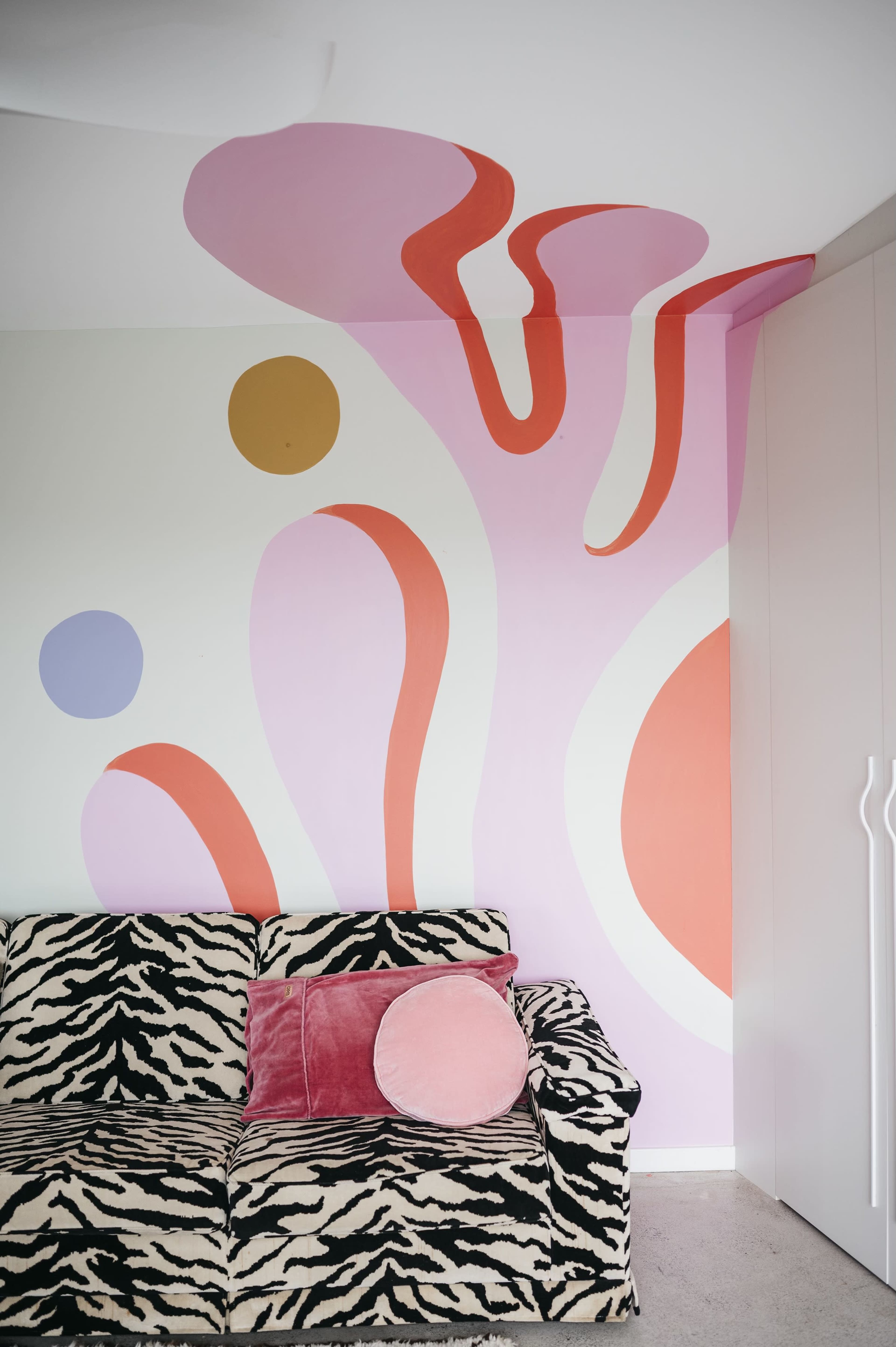 A couch with a zebra print pattern in front of a wall adorned with colorful, abstract shapes in pastel tones.