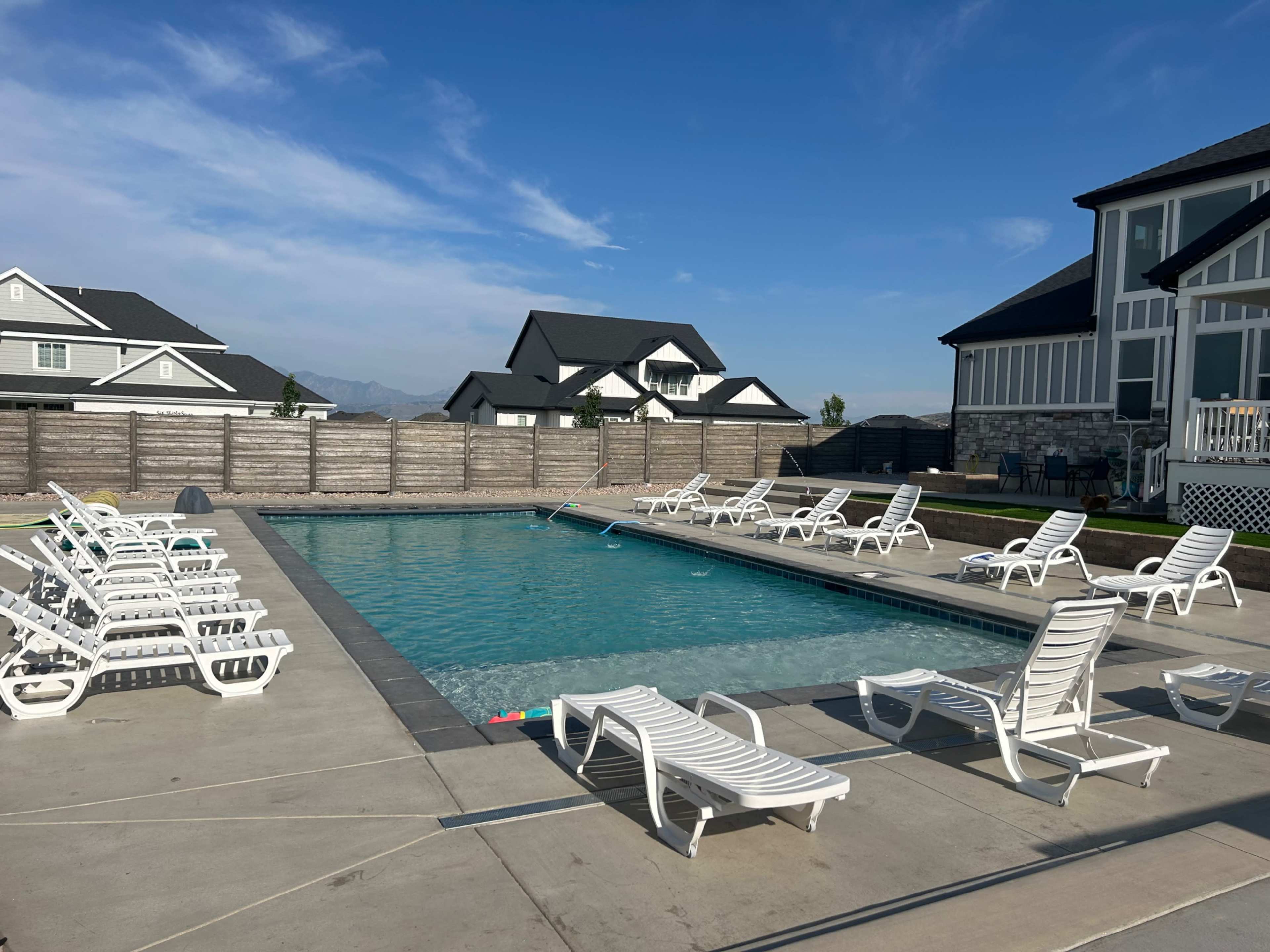A swimming pool surrounded by white lounge chairs and residential buildings in the background.