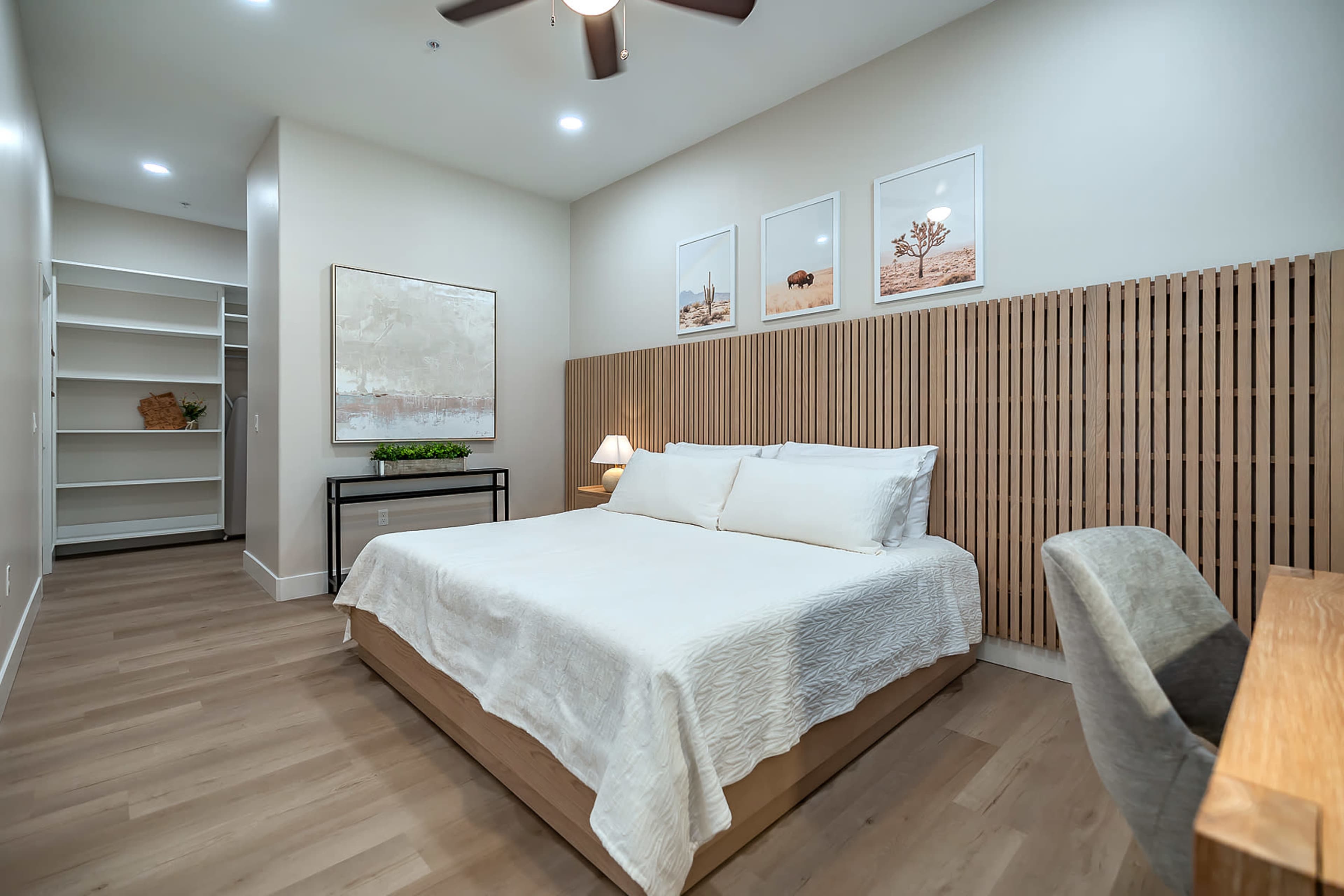 A modern bedroom with a bed, a wooden feature wall, and a small desk, accompanied by a built-in closet and framed artwork on the wall.