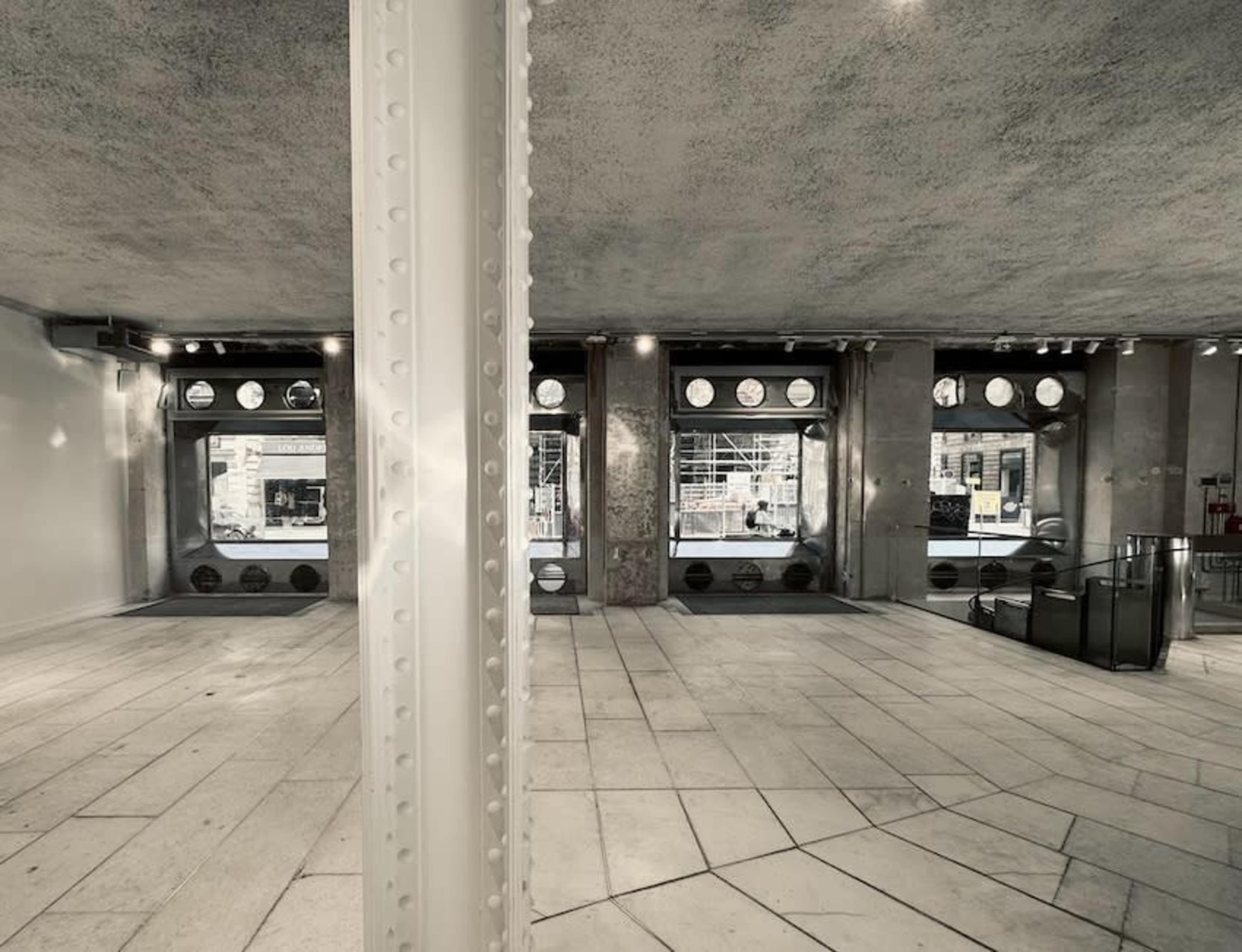 The image shows an empty, modern retail space with large windows and concrete columns.