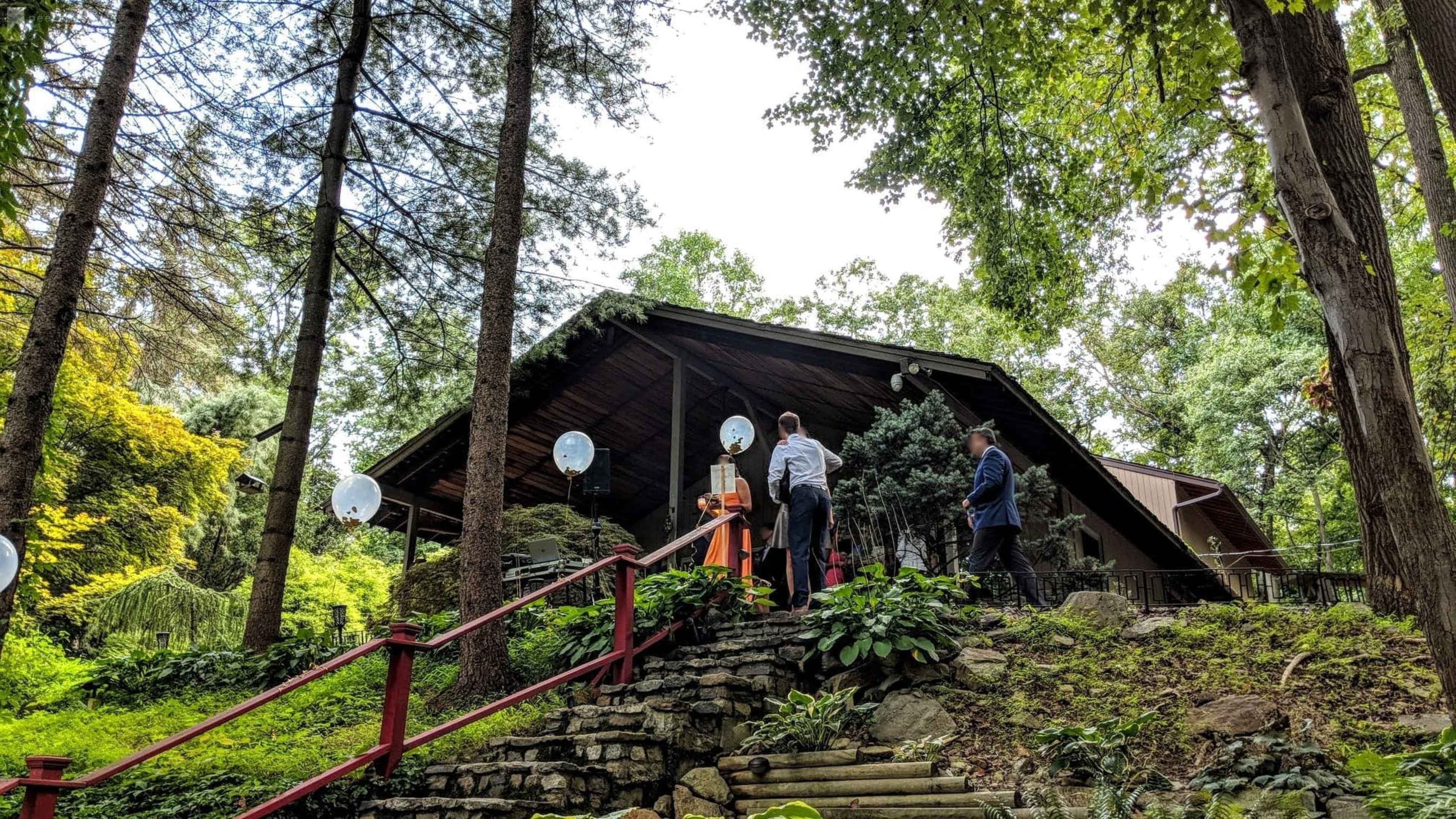 A group of people stands on a stone path leading to a rustic building surrounded by trees.