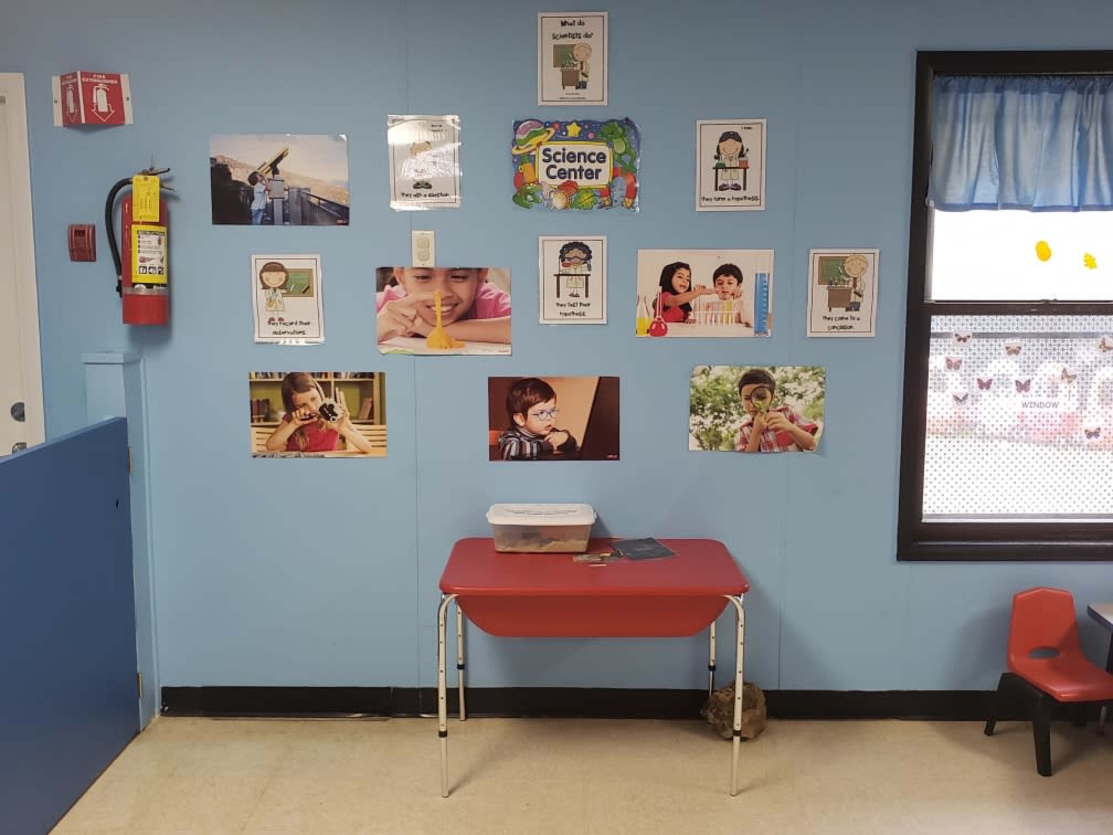 A classroom wall decorated with various educational posters and a red table in front.