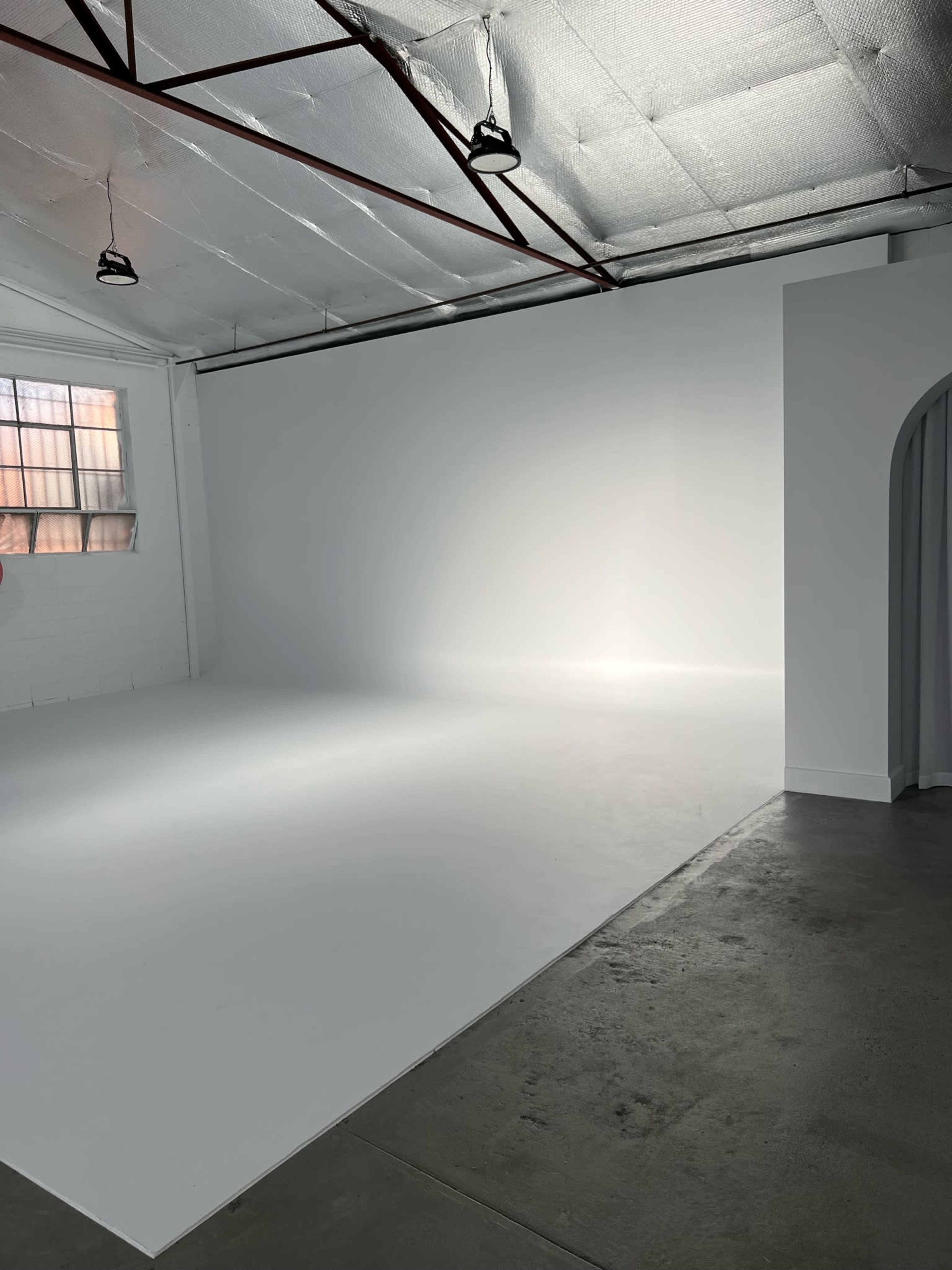 A spacious, empty studio with a white background and concrete flooring.