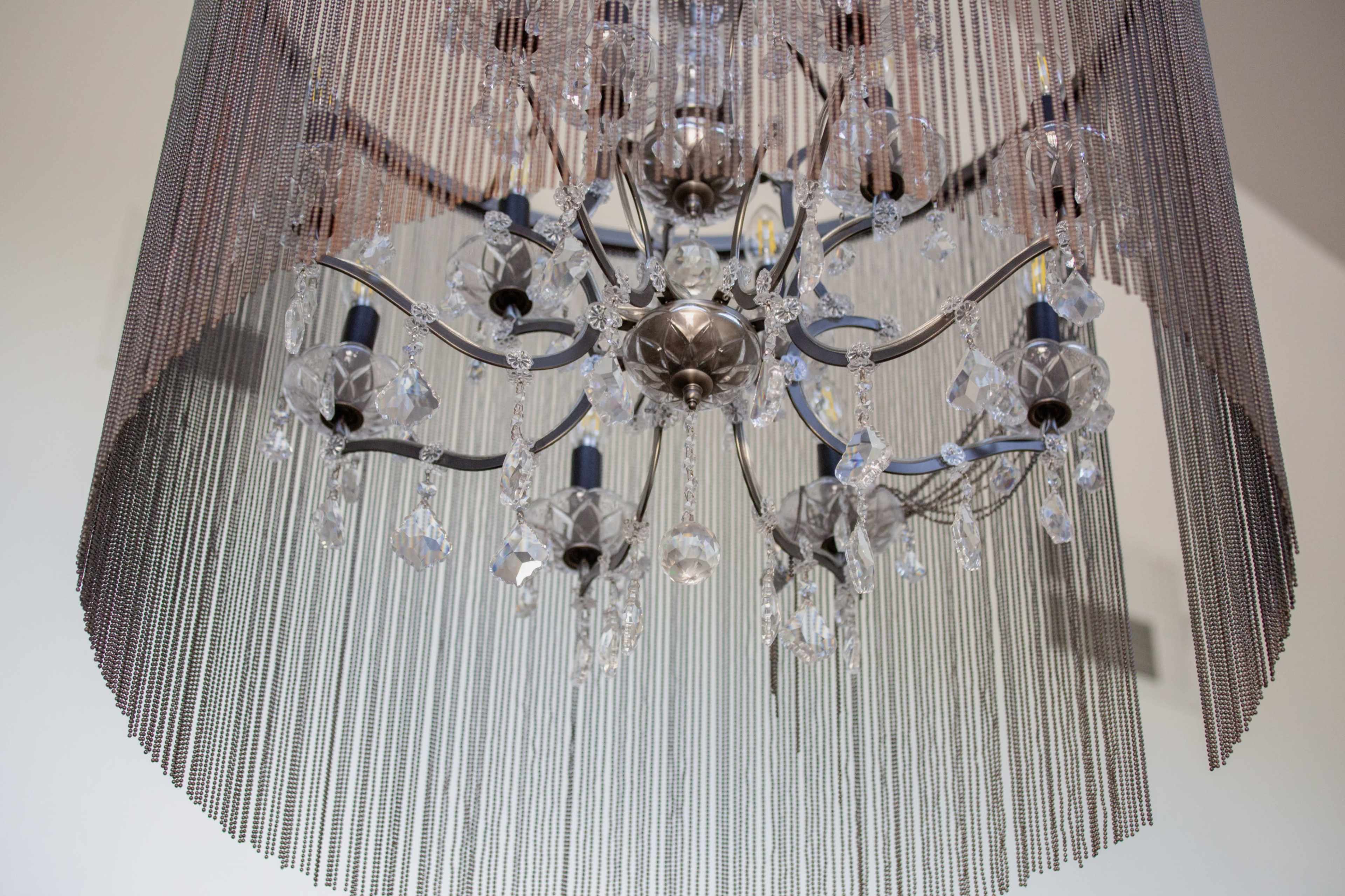 The image shows a decorative chandelier made of metal and glass hanging from a ceiling, surrounded by strands of chains.