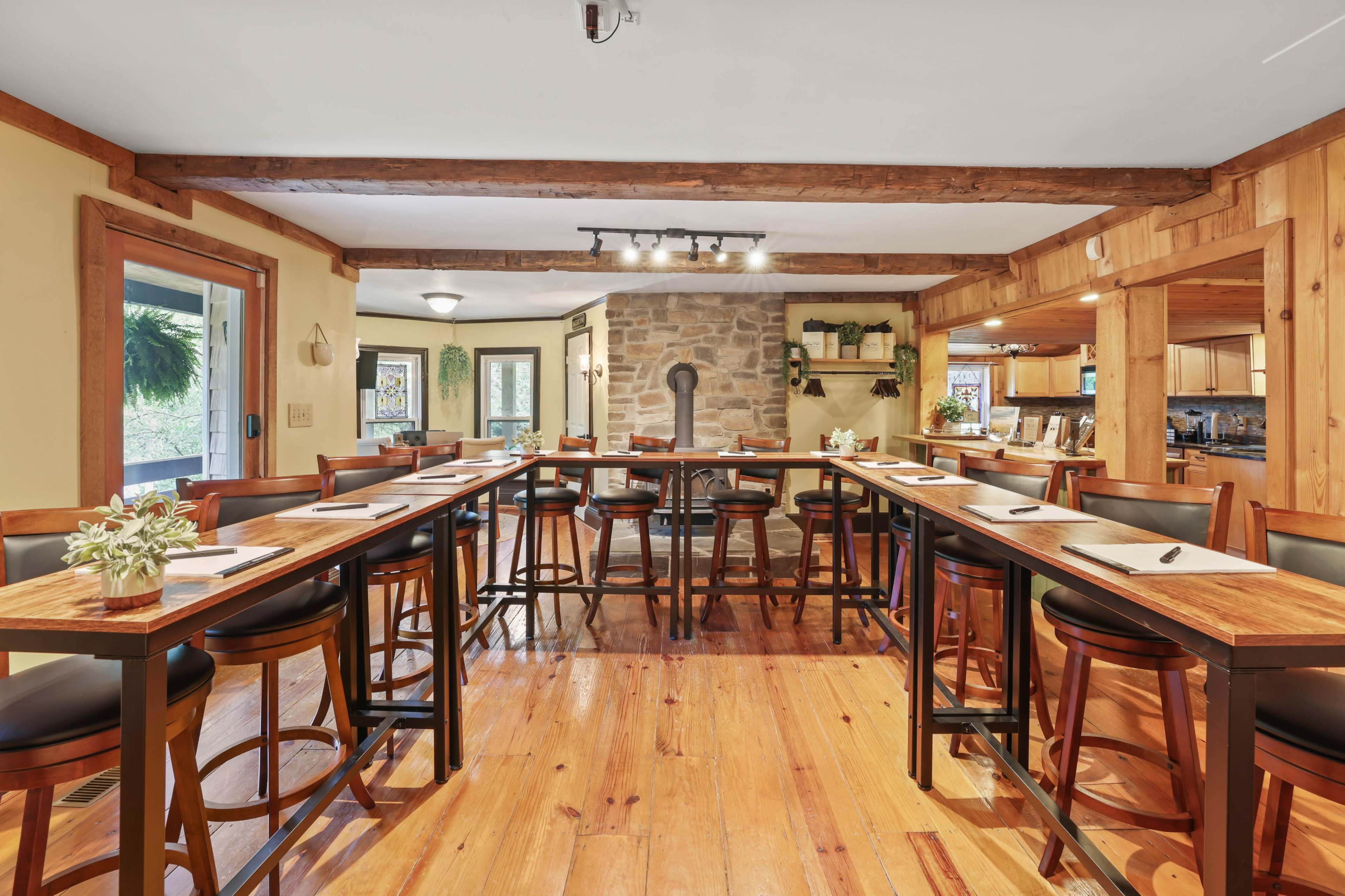 A spacious dining area with a long table and high-backed chairs, illuminated by overhead lights and featuring a stone fireplace in the background.
