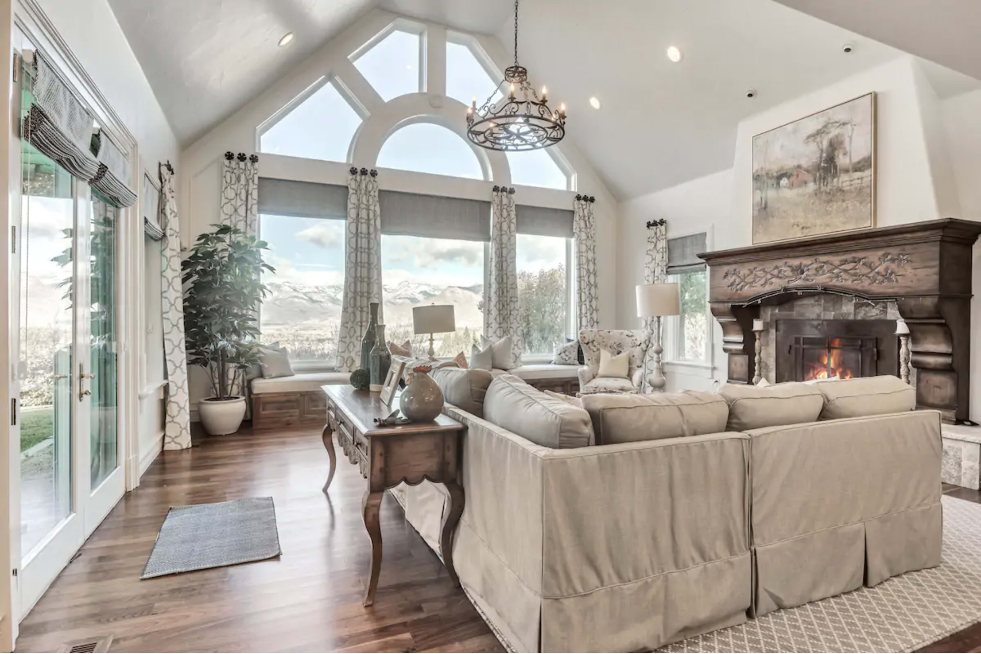 A cozy living room with large windows, a stone fireplace, and a comfortable sectional sofa.