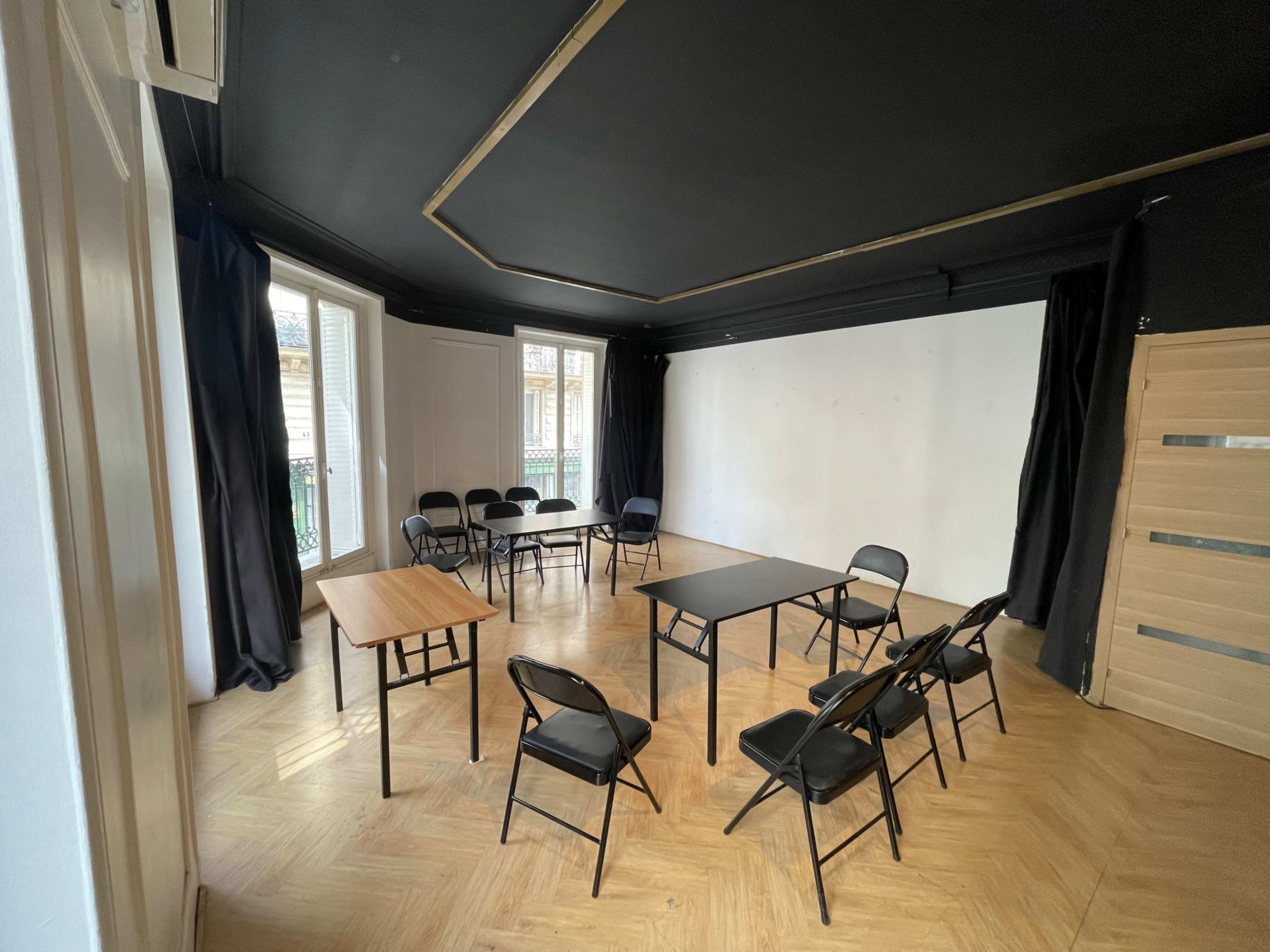 The image shows a room with a black ceiling, white walls, and several tables and chairs arranged in a circular layout.